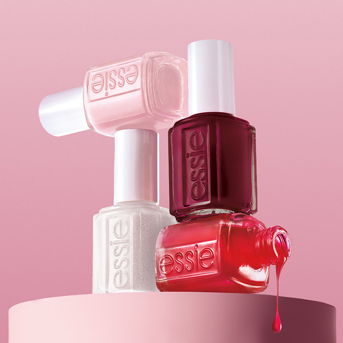 Fyra Essie-nagellack i rosa nyanser mot rosa bakgrund; lack droppar från en flaska.
