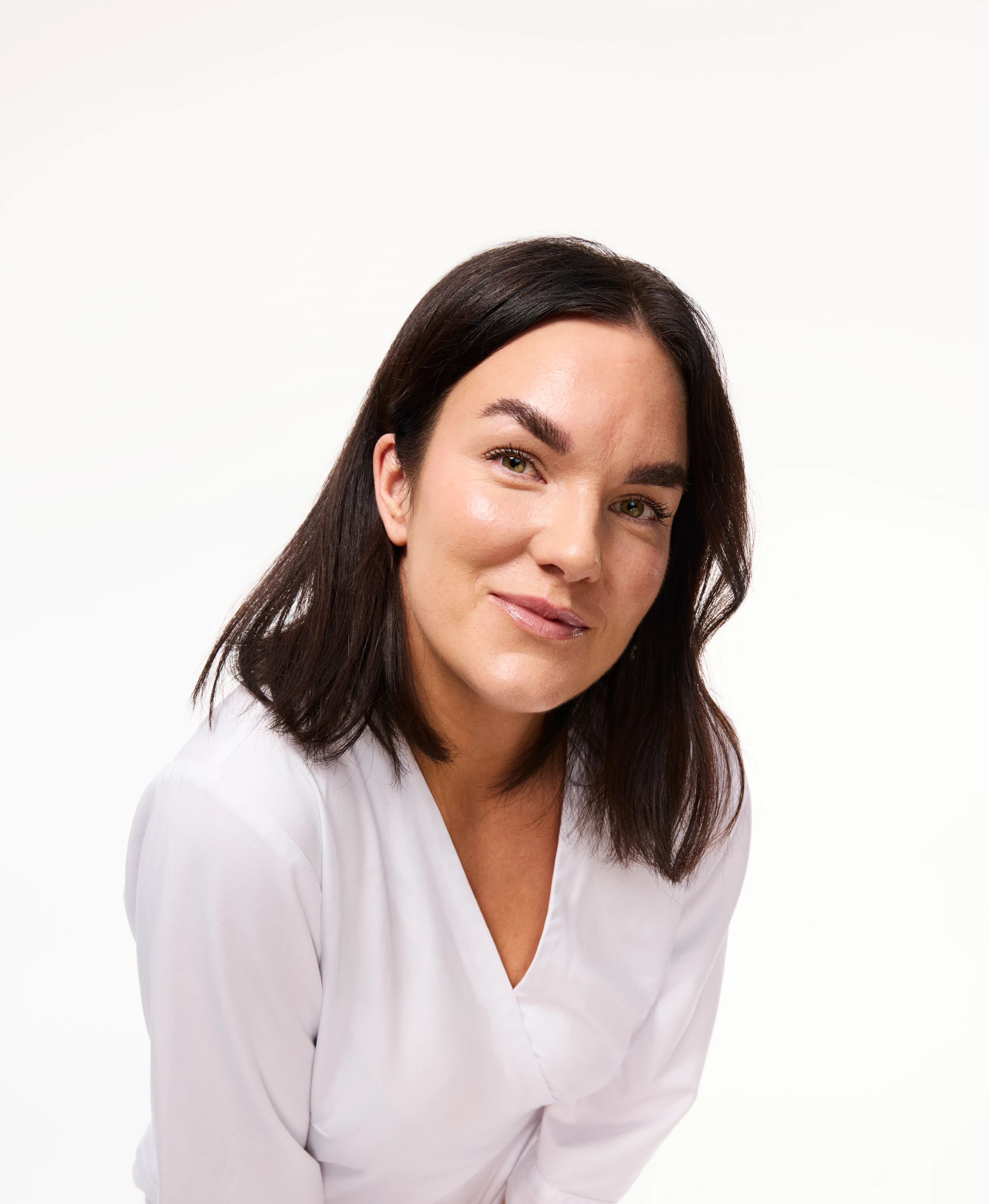 En person med mørkt hår og hvit skjorte står mot en hvit bakgrunn.