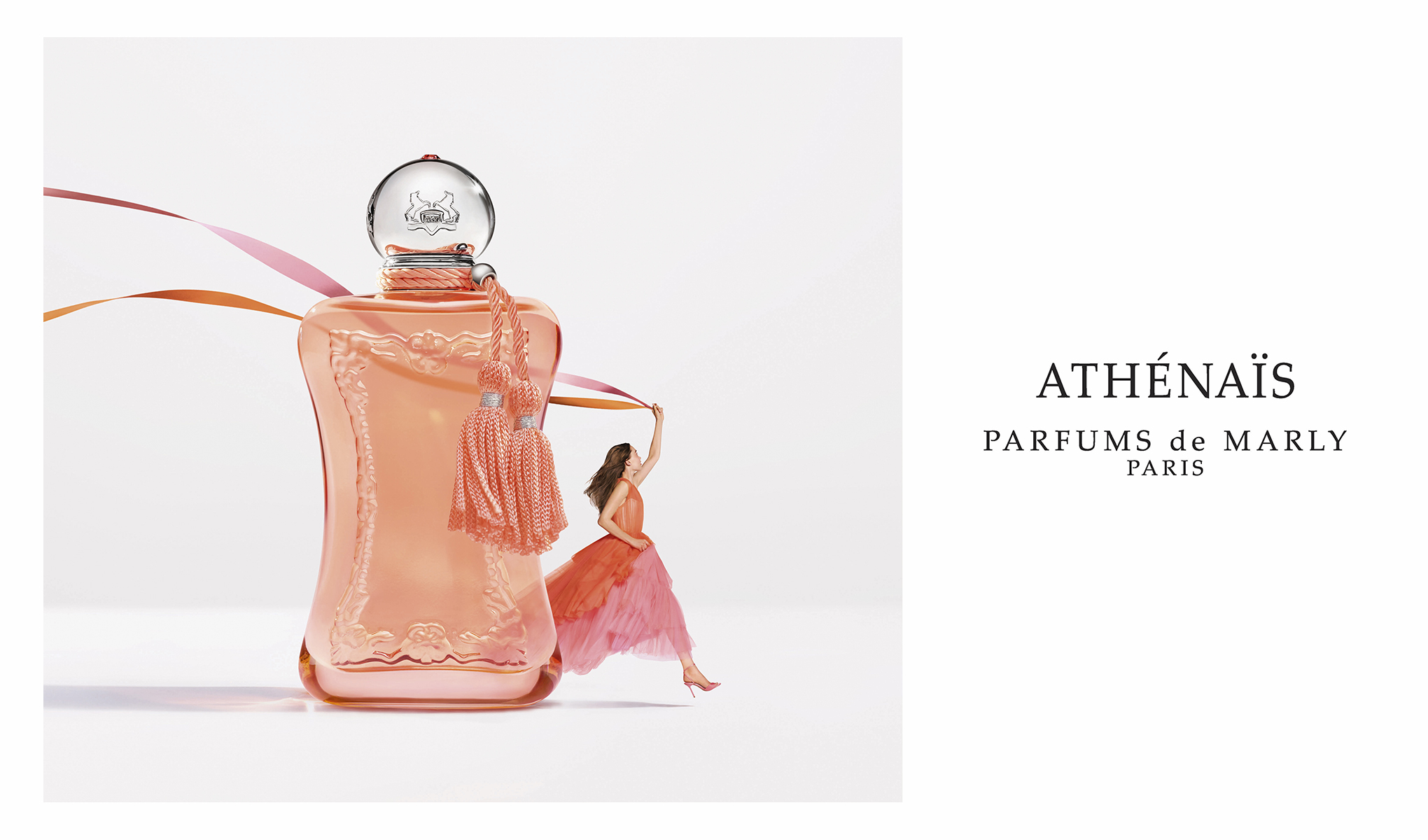 Stor rosa parfymflaska med dekorativ form och tofs, bredvid en person i rosa klänning som håller färgade band, mot ljus bakgrund med texten “ATHÉNAÏS PARFUMS de MARLY PARIS”.