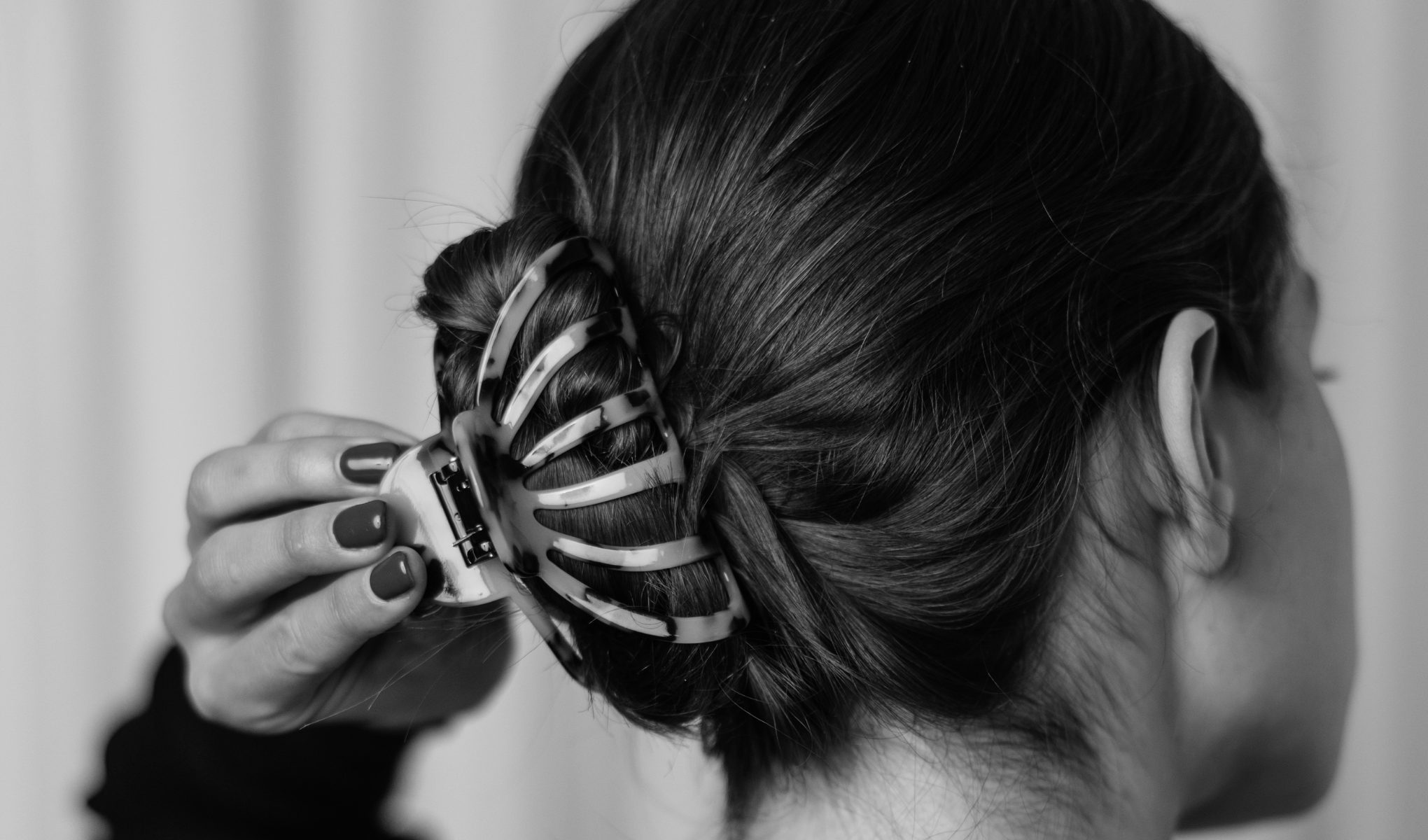 Henkilö, jolla on ruskeat hiukset, käyttää hiusklipsiä pitämään hiuksensa ylhäällä. Klipsi on mustavalkoinen ja näyttää olevan muovia.