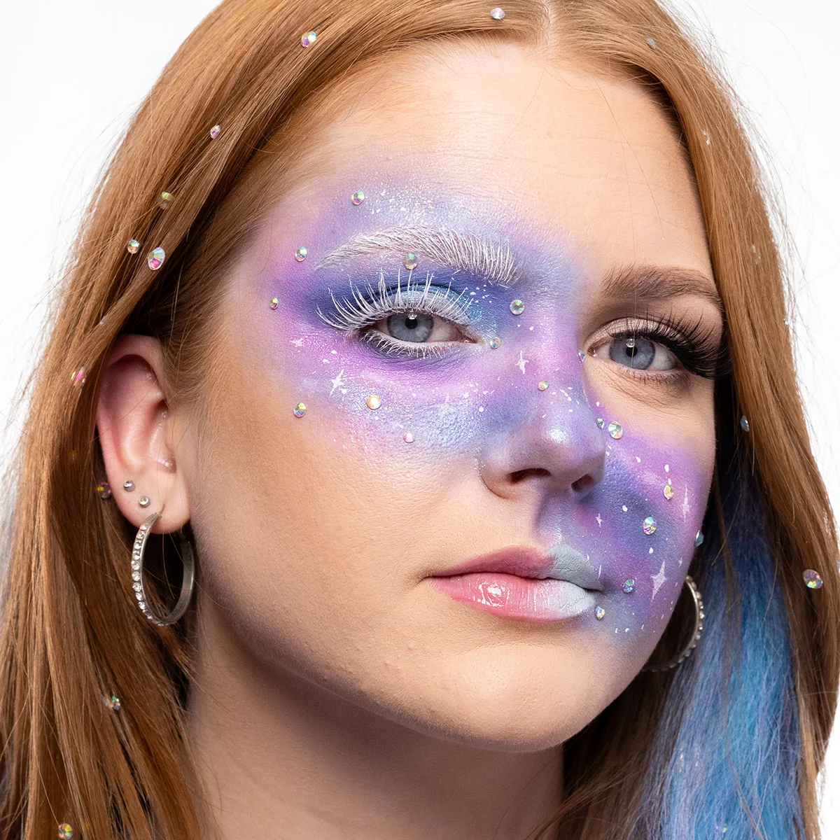 Närbild av en person med rött hår dekorerat med små pärlor och blå slingor. Personen har flera örhängen, inklusive en stor ring.