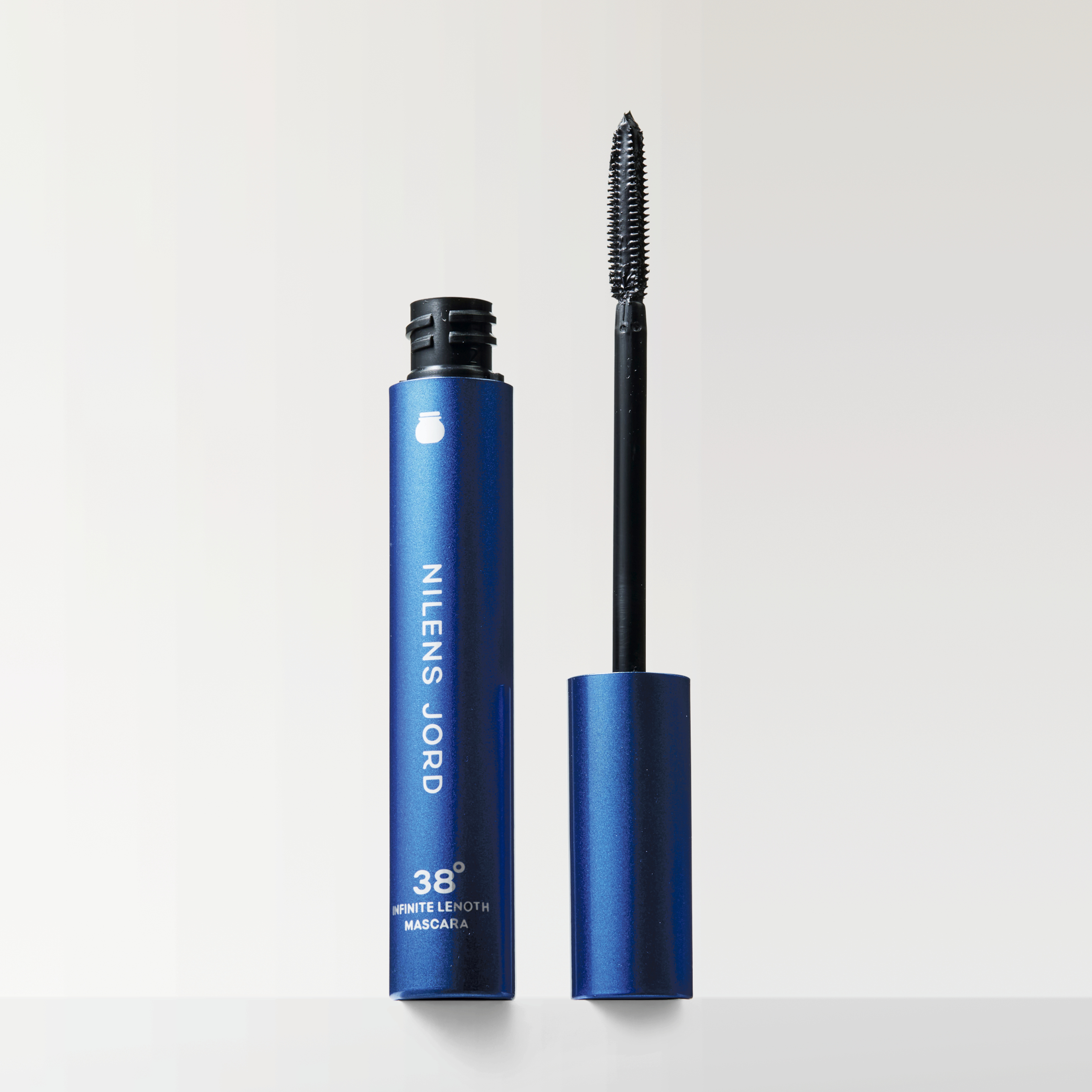 En öppen blå mascaraförpackning från Nilens Jord med borste bredvid, mot en ljus, neutral bakgrund.