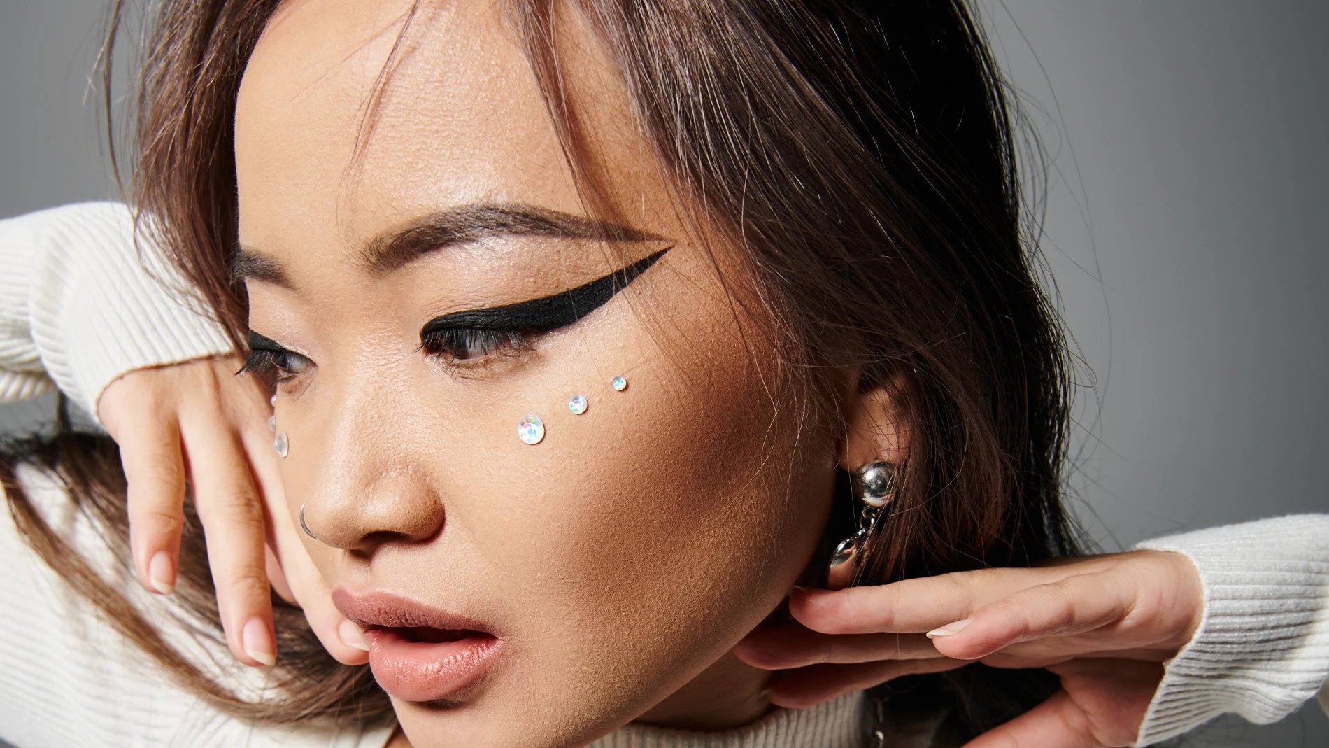 Kvinne med dramatisk eyeliner, rhinestone ansiktsperler og stilig tilbehør.