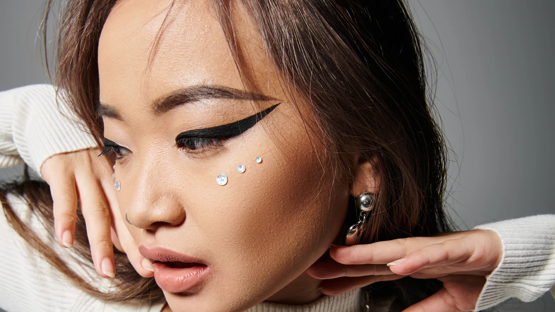 Kvinne med dramatisk eyeliner, rhinestone ansiktsperler og stilig tilbehør.