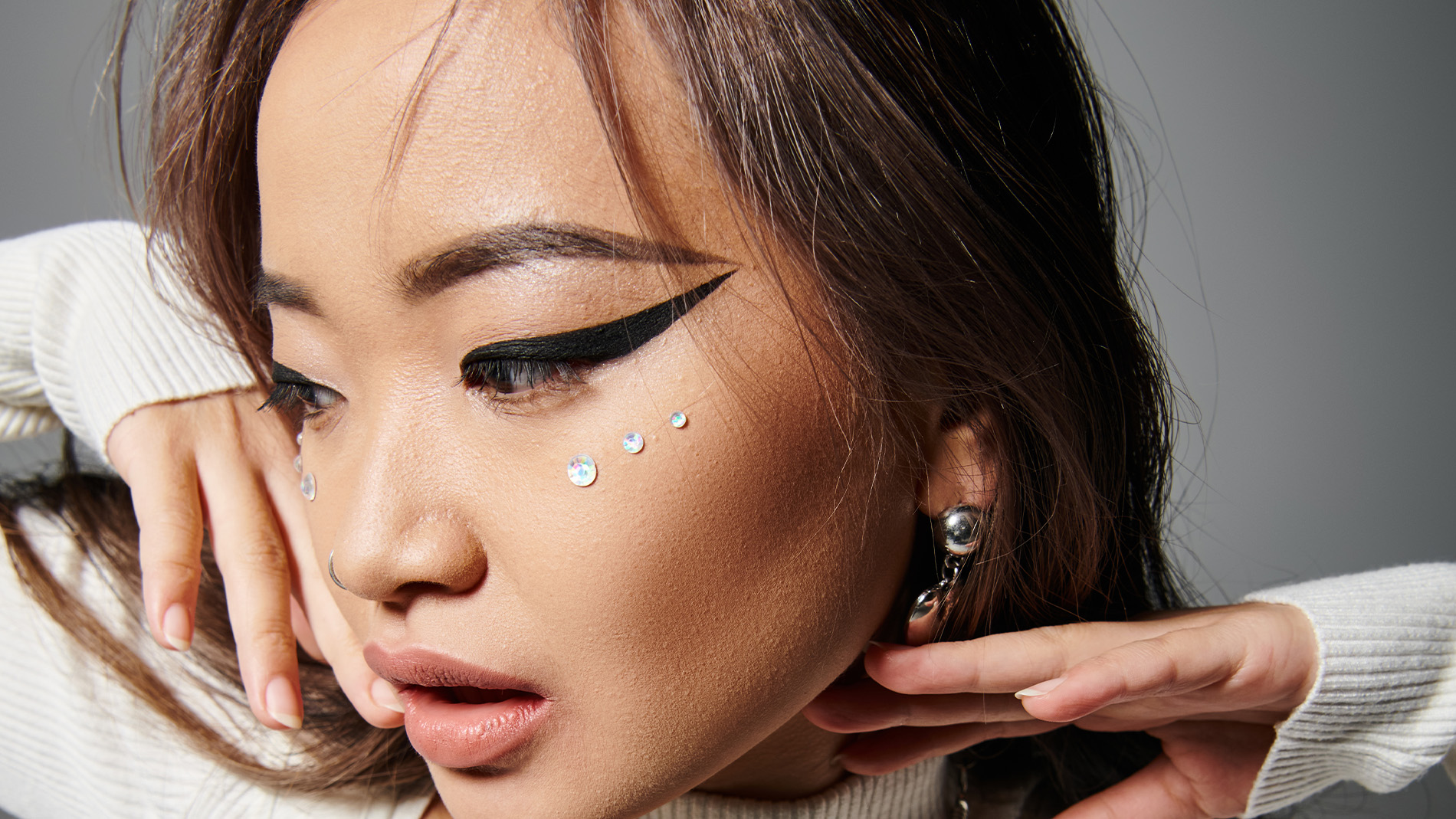 Kvinna med dramatisk eyeliner, ansiktsstenar i strass och snygga accessoarer.