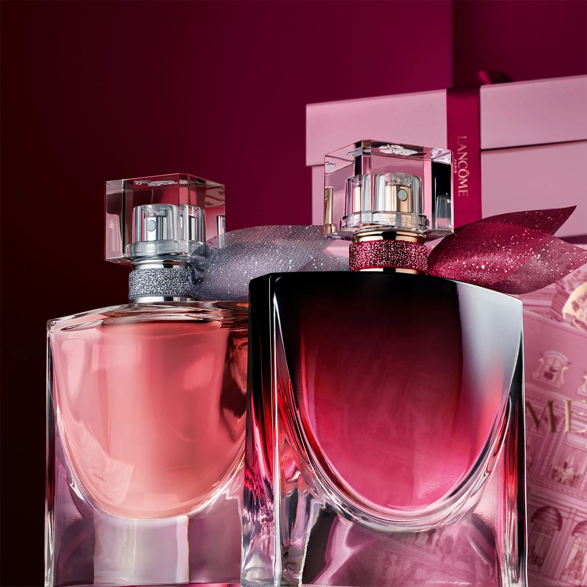 To parfymeflasker. Den ene er rosa med sølvdetaljer, den andre er mørkerød med et glitrende rødt bånd.