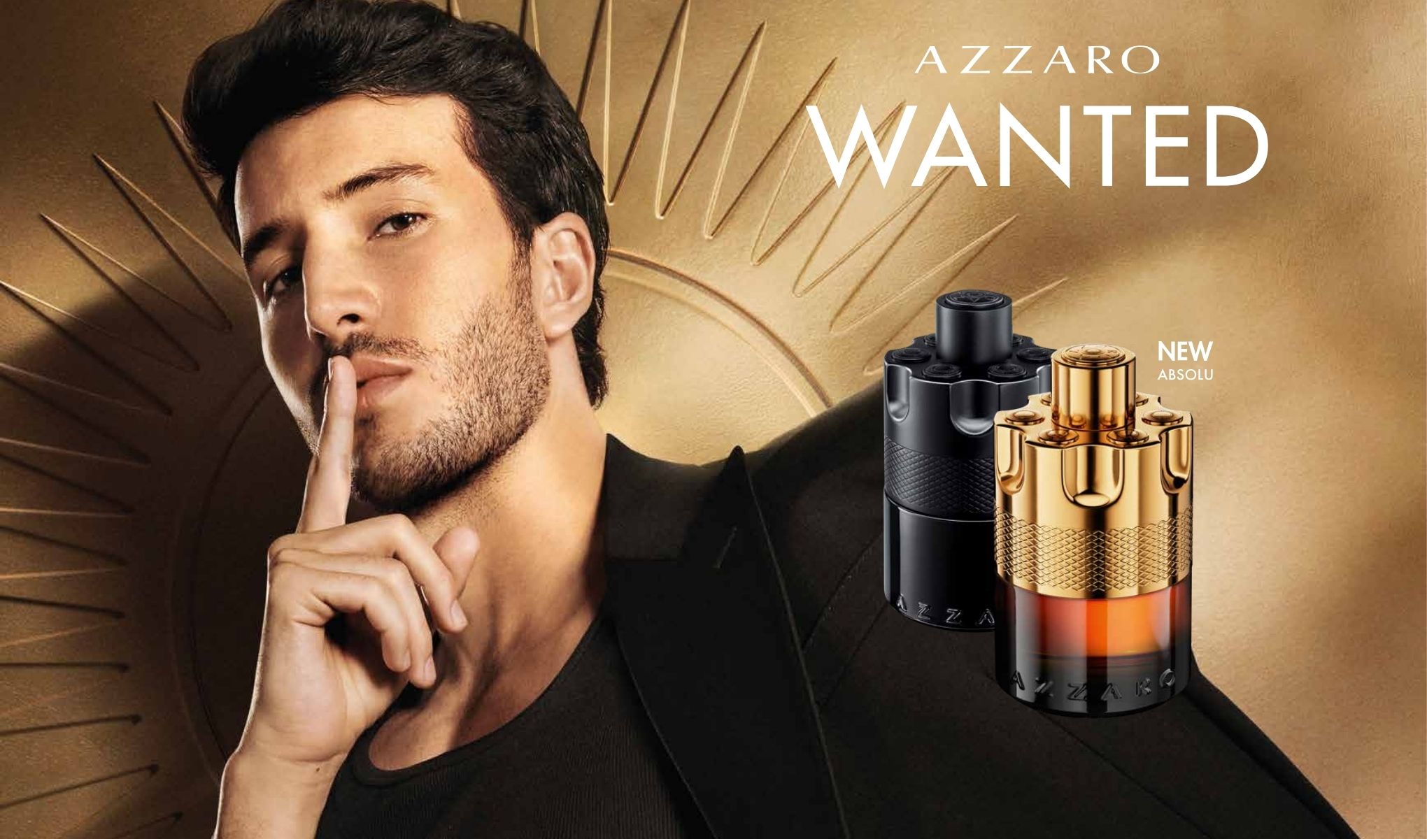 En man med fingret vid munnen. Bredvid honom står två parfymer, en i guldförpackning och en i svart förpackning.