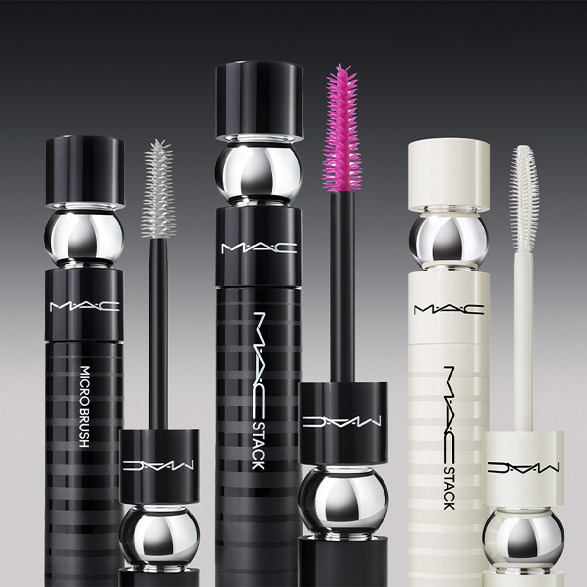 Neljä erilaista MAC Cosmeticsin ripsiväriä on rivissä tummanharmaalla pohjalla. Pakkaus on mustavalkoinen hopeisilla yksityiskohdilla, ja MAC-logo näkyy selvästi jokaisessa ripsivärissä. Harjat ovat erivärisiä.