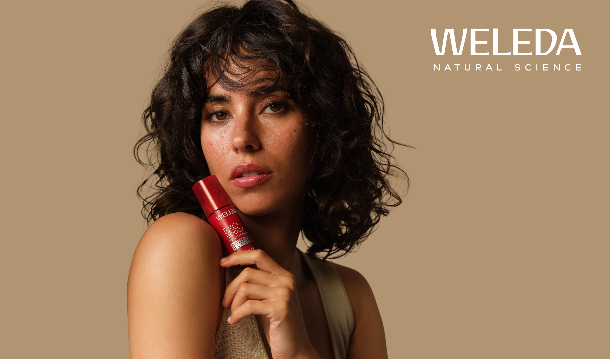 Kvinne holder rød Weleda Exo Boost Youth Power Night Elixir 30ml flaske. Weleda Natural Science-logo.