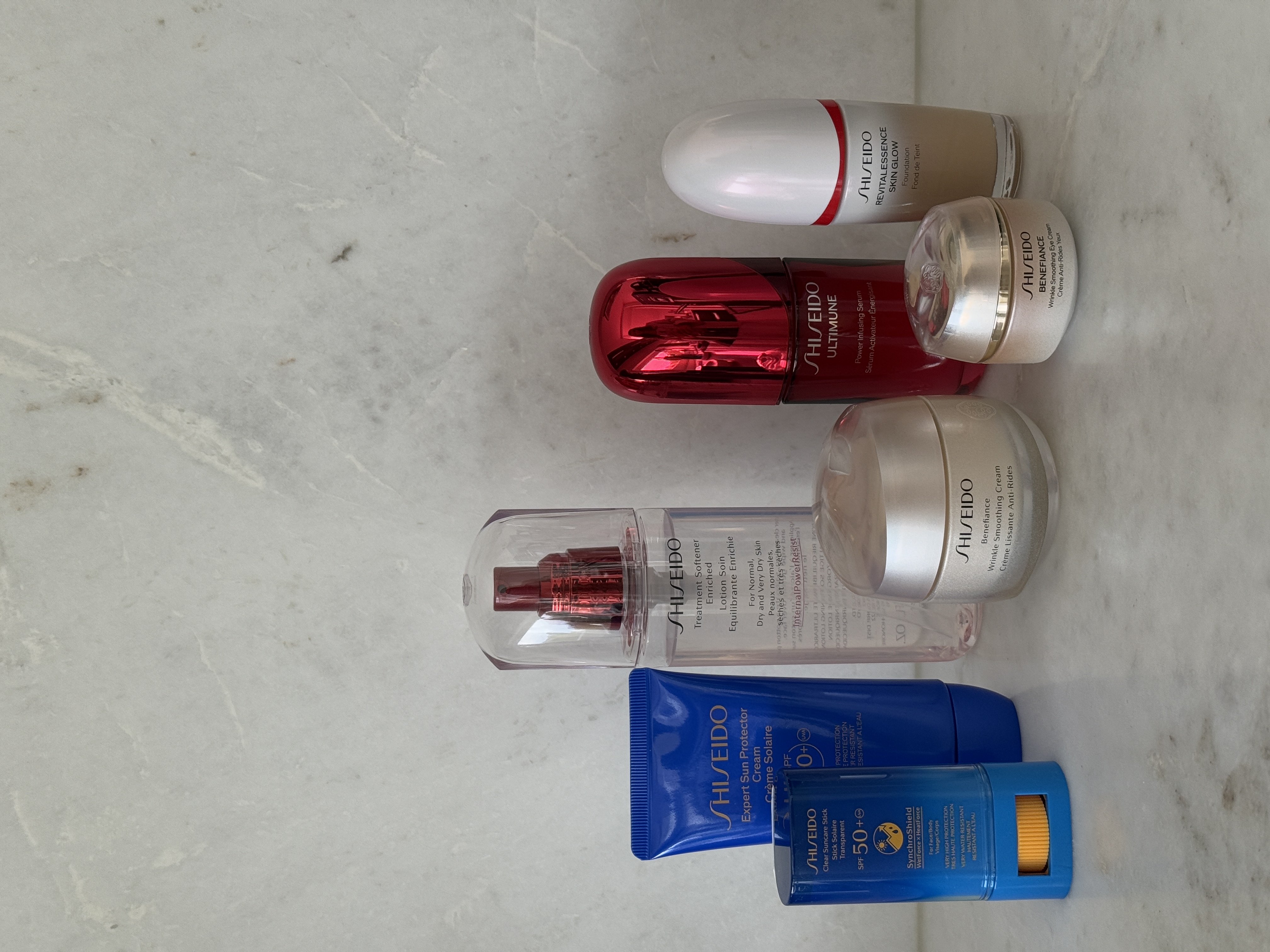 En samling av Shiseido hudpleieprodukter inkludert serum, ansiktskrem og solbeskyttelse, arrangert på en marmoroverflate.