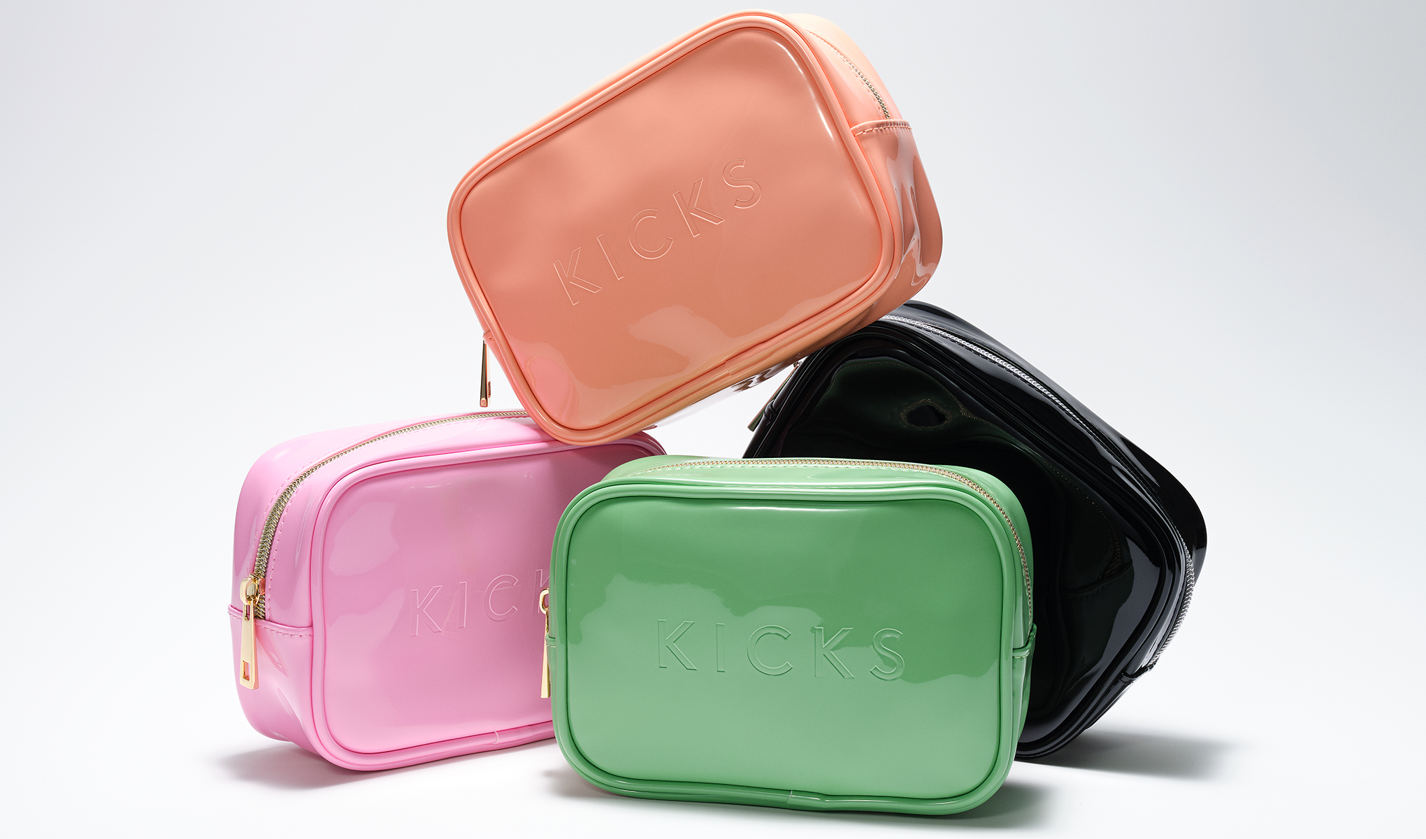 Fyra necessärer från KICKS i olika färger: rosa, grön, svart och persikofärgad. De är staplade på varandra mot en vit bakgrund. Varje necessär har texten "KICKS" präglad på framsidan.