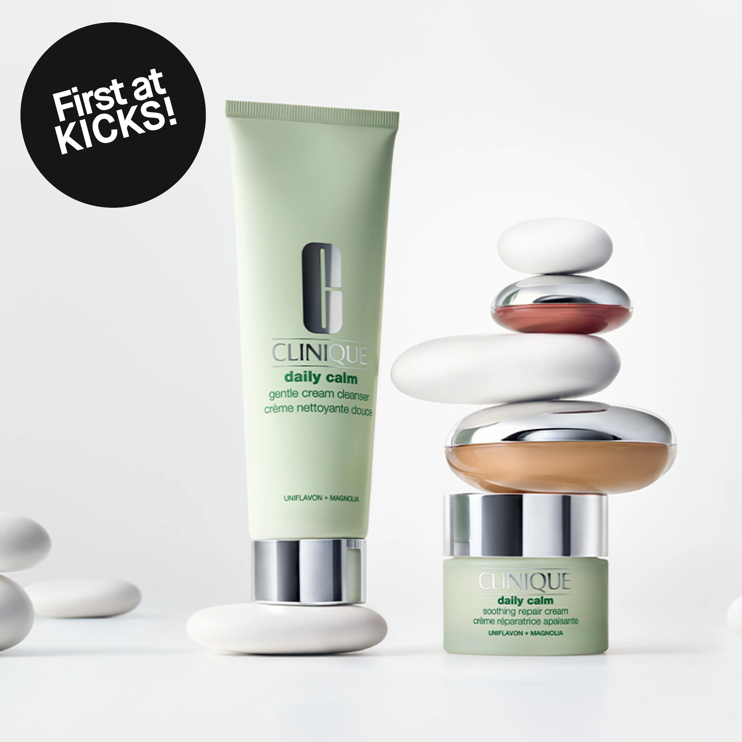 Clinique Daily Calm-rens og ansiktskrem mot lys bakgrunn ved siden av balanserte steiner. Bildet inneholder teksten «First at KICKS!».