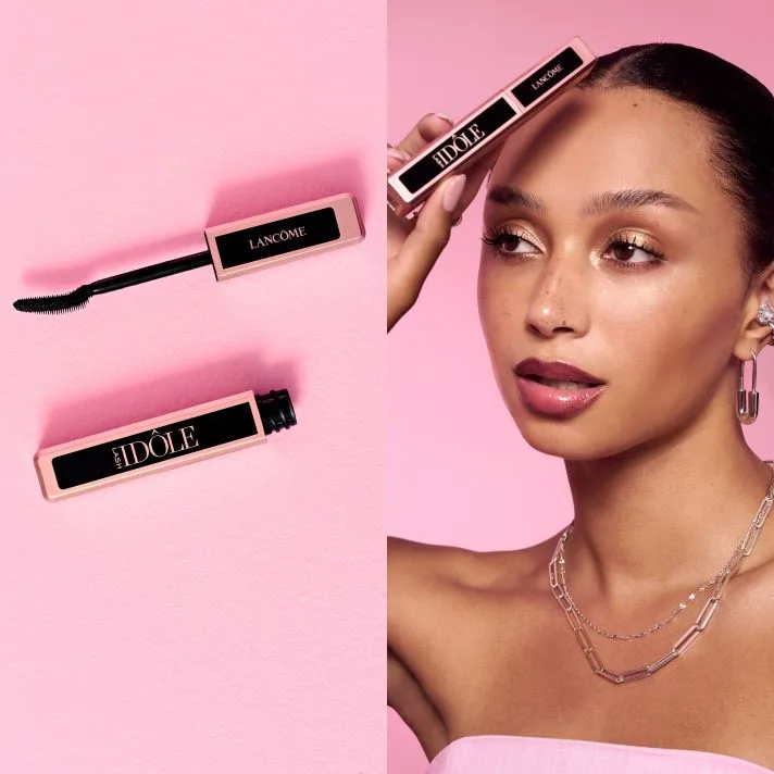 Lancôme Lash Idôle mascara vises åpen med børste og hylse samt en person som holder produktet mot ansiktet mot rosa bakgrunn.
