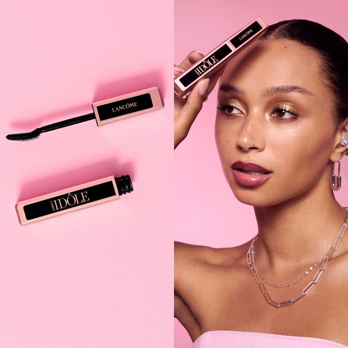 Lancôme Lash Idôle -ripsiväri avoimena harjan ja hylsyn kanssa sekä henkilö, joka pitää tuotetta kasvojen lähellä vaaleanpunaisella taustalla.