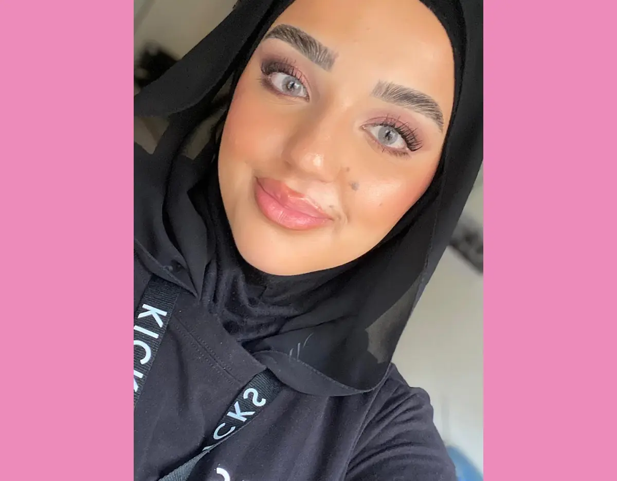 Kvinne med hijab og sminke som smiler til kameraet, med en rosa ramme.