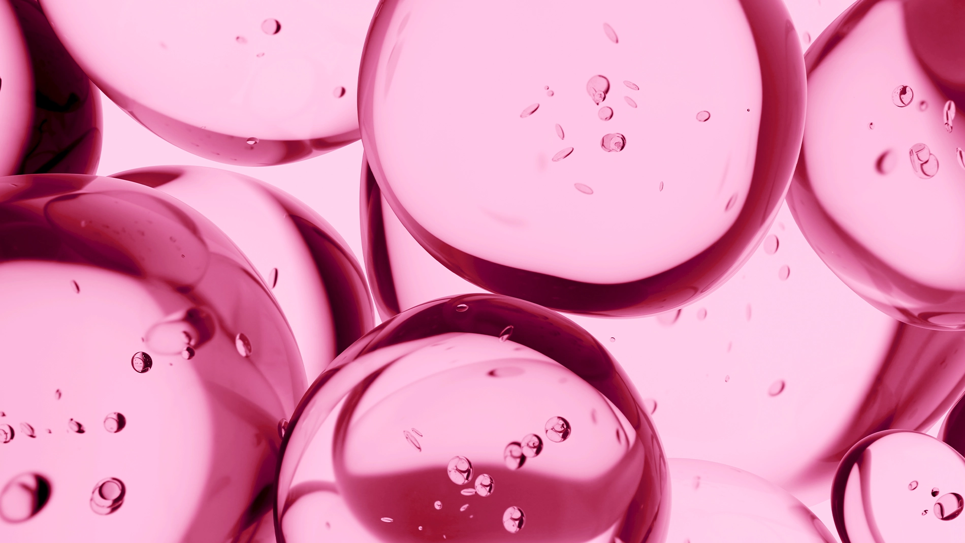 Närbild av genomskinliga rosa gelbubblor med små luftbubblor inuti, placerade tätt intill varandra mot ljus bakgrund. Blank, glansig yta med reflektioner som framhäver vätskans struktur.