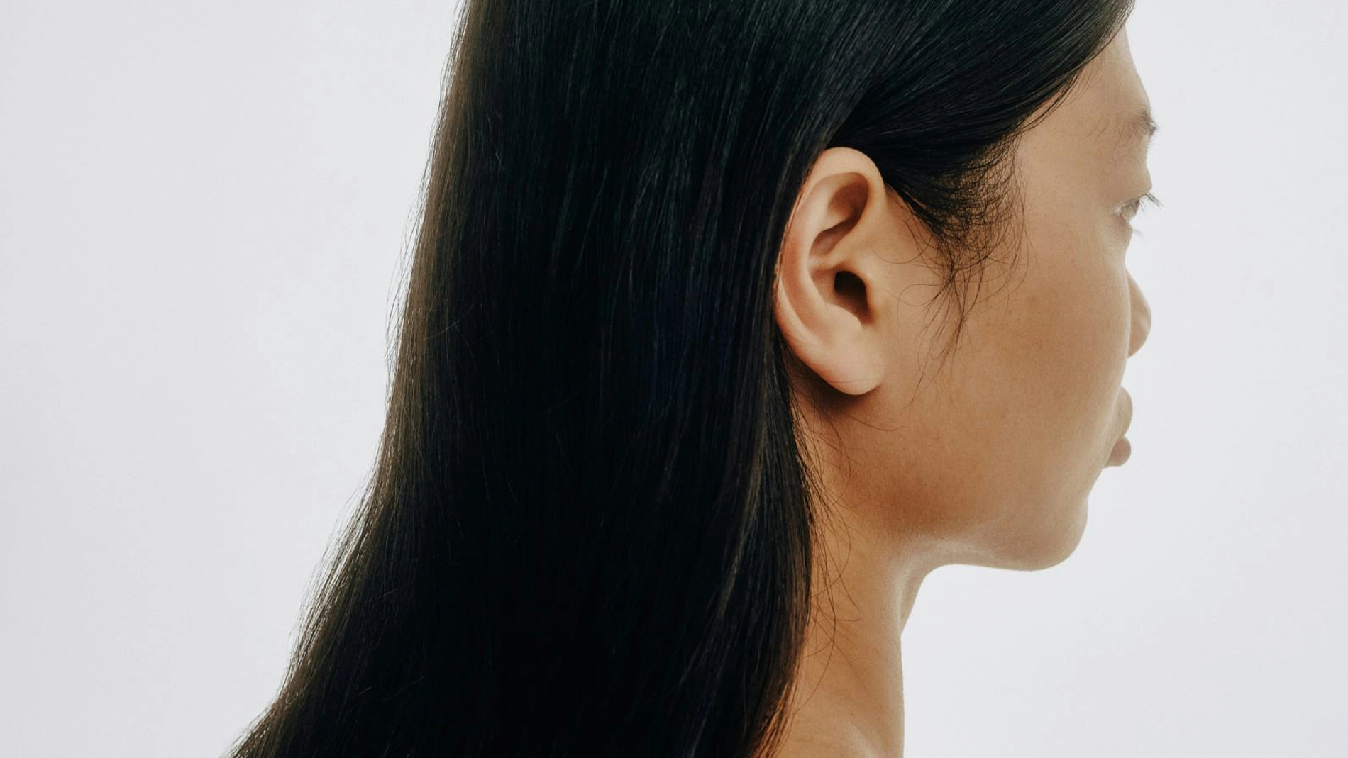 Profilbild av en person med långt, rakt mörkt hår mot ljus bakgrund, med fokus på hårets glans och släta struktur för hårvård.