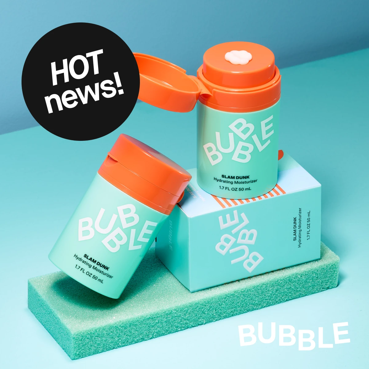 To Bubble Slam Dunk fuktighetskremer i turkis emballasje med oransje lokk, hvor én står åpen med krem synlig. Produktene er plassert dekorativt på en farget sokkel mot lyseblå bakgrunn.