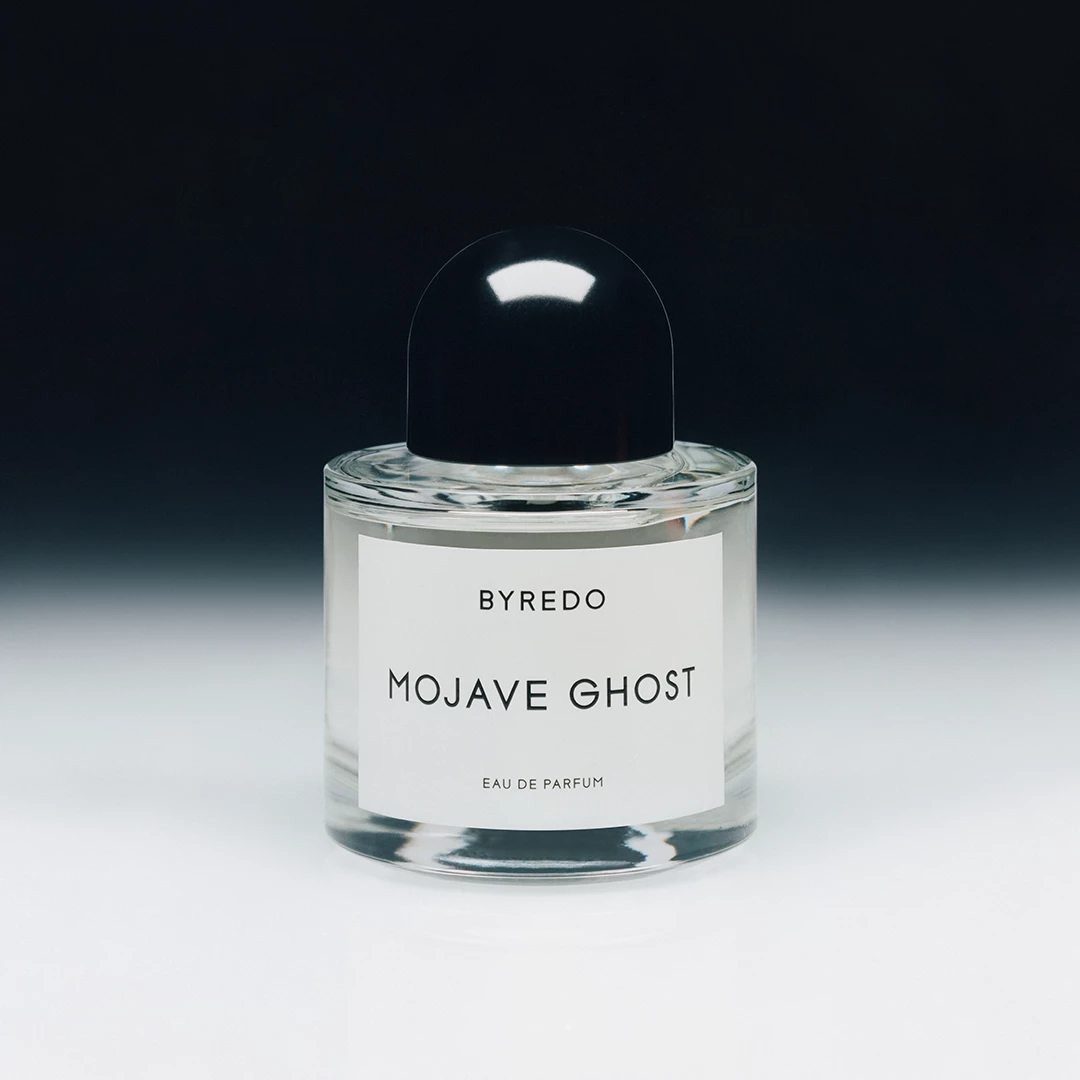 Parfymflaska från Byredo med namnet "Mojave Ghost". Flaskan har en svart kork och en vit etikett med svart text. Bakgrunden är mörk och övergår gradvis till ljusare nyanser.