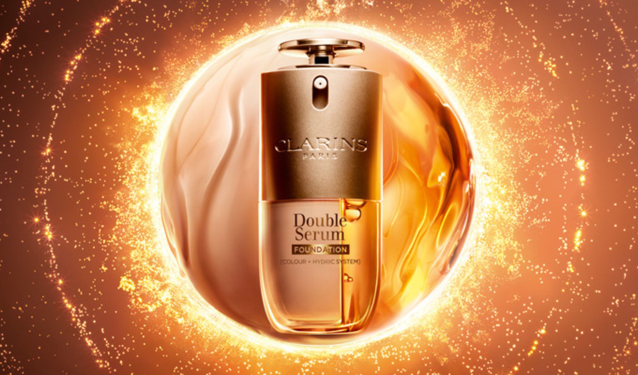 Kultainen Clarins Double Serum Foundation -meikkivoidepullo, jossa pumppukorkki. Pullo on keskellä hehkuvaa, kultasävyistä valokehää ja taustalla on lämpimän oranssi, kimaltava efekti.