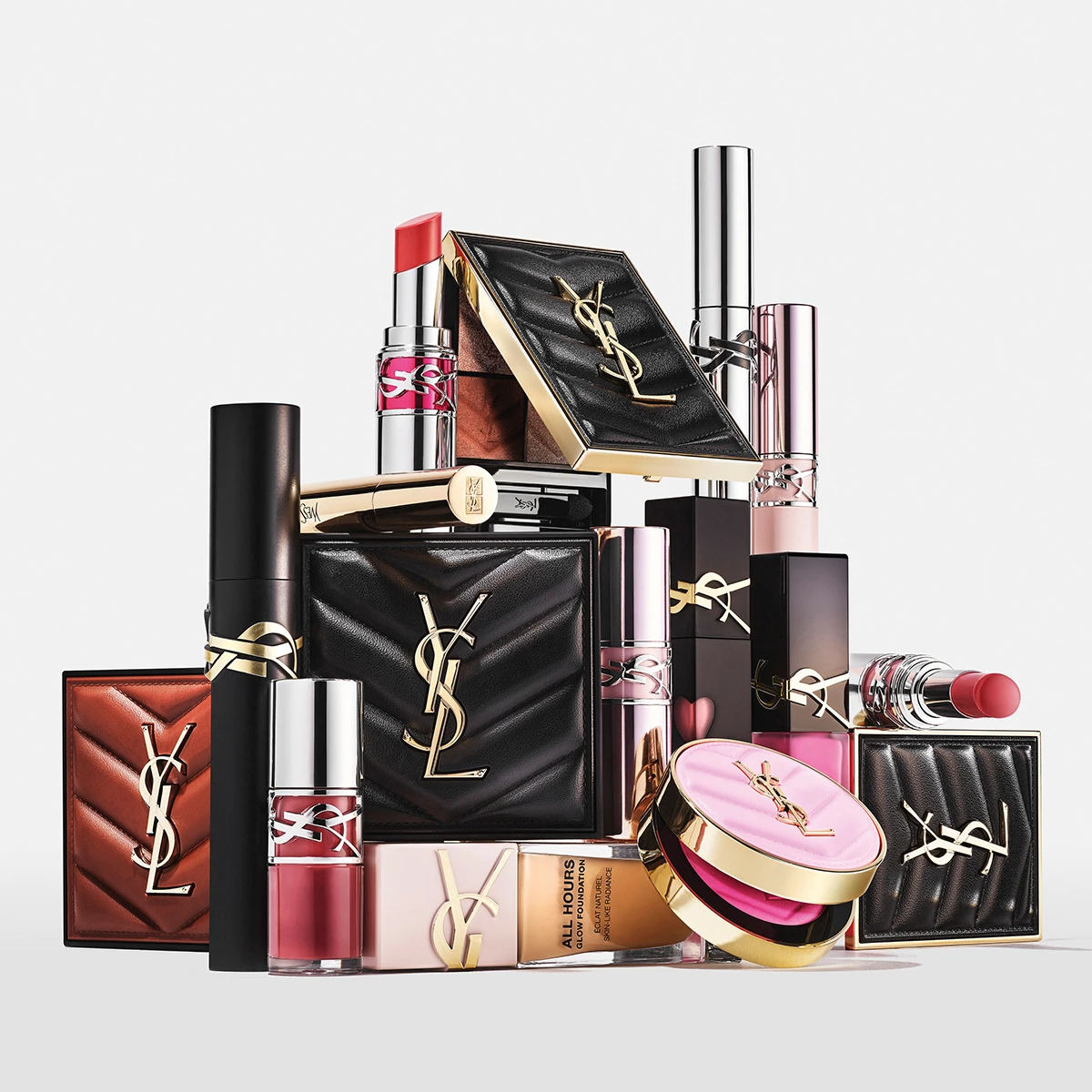 YSL sminkeprodukter: leppestifter, vatterte pudderdåser og "ALL HOURS GLOW FOUNDATION" i svart og gull forpakning.