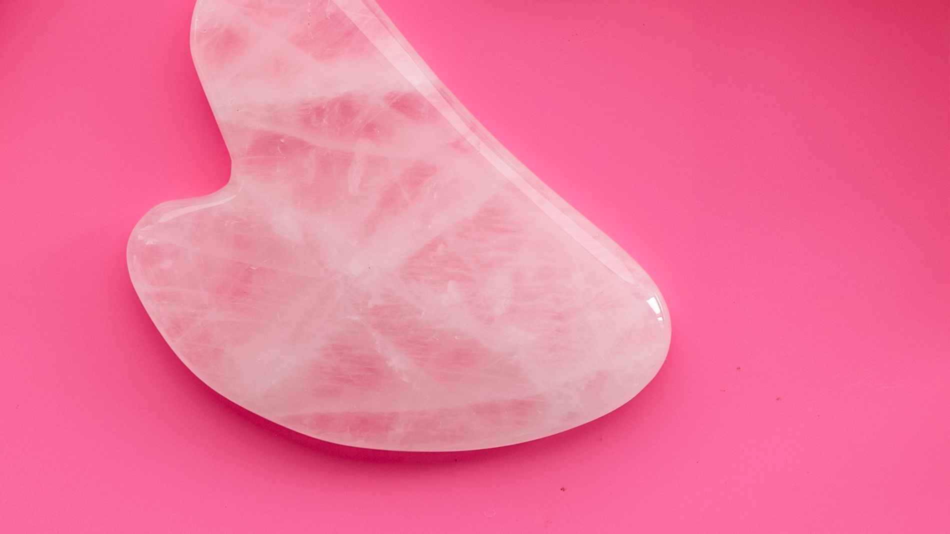 Rosa hjerteformet gua-sha-stein mot cerise bakgrunn.