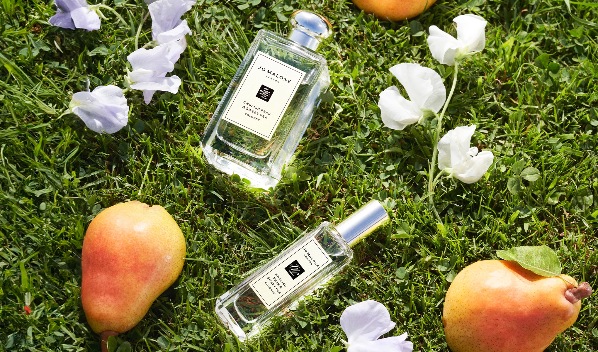 Kaksi Jo Malone Londonin hajuvesipulloa makaa ruohikolla, jossa on valkoisia kukkia ja kaksi päärynää niiden ympärillä. Pullot on merkitty "English Pear & Sweet Pea Cologne".