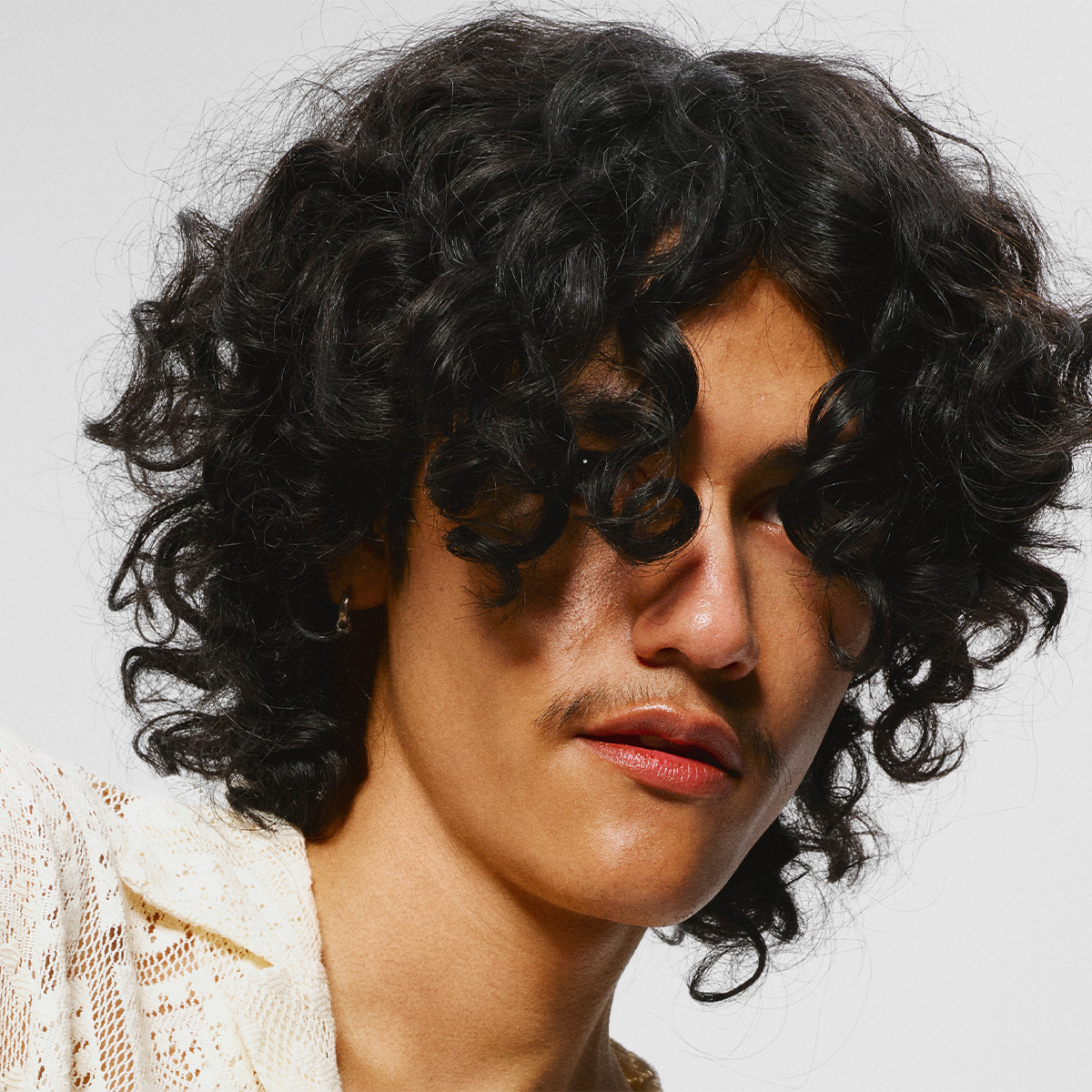 En man med lockigt hår som faller över ögonen, mot en grå bakgrund.