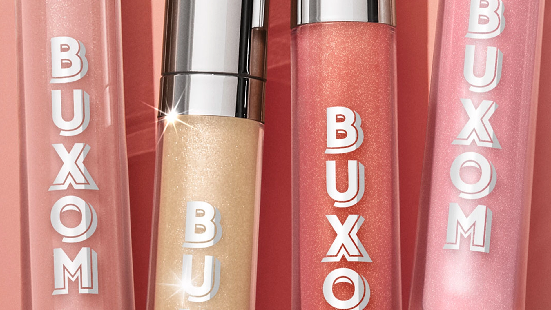 Fire lipgloss i forskjellige farger med merket BUXOM mot en rosa bakgrunn.