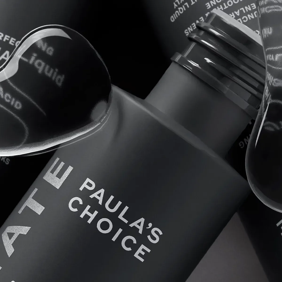 tre produkter av Paula's Choice i närbild med grå bakgrund och vattendroppar i förgrund