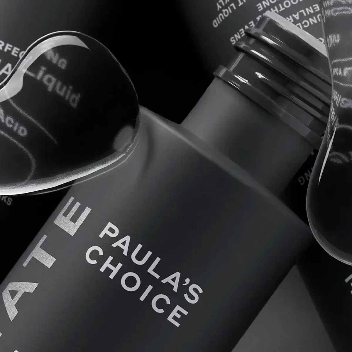 Tre produkter fra Paula's Choice i nærbilde med grå bakgrunn og vanndråper i forgrunnen.