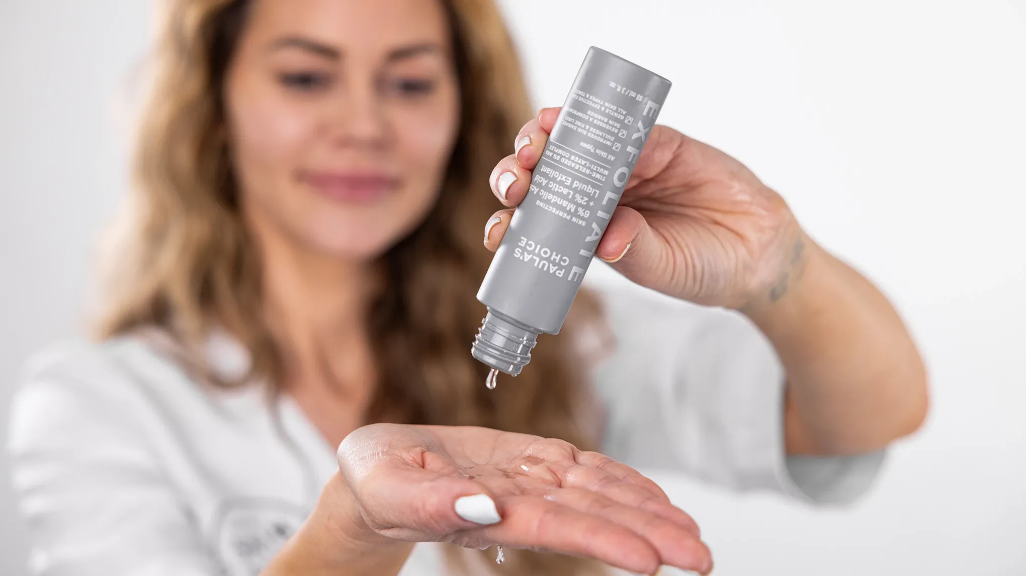 Kvinna häller flytande exfoliering från en grå flaska i handen
