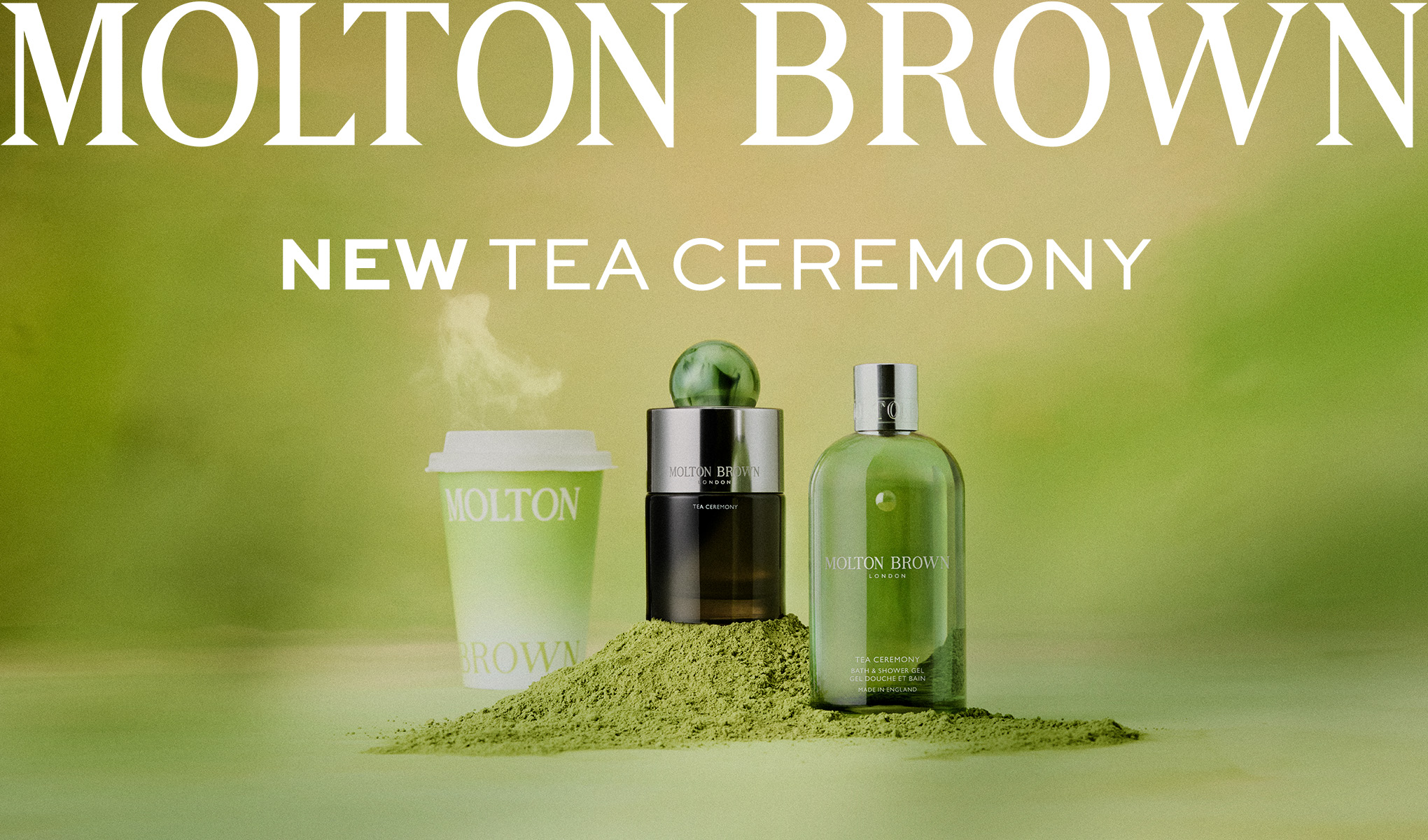 Molton Brown Tea Ceremony-produkter mot grön bakgrund: doft, duschgel och en ångande takeaway-mugg placerad på grönt tepulver.