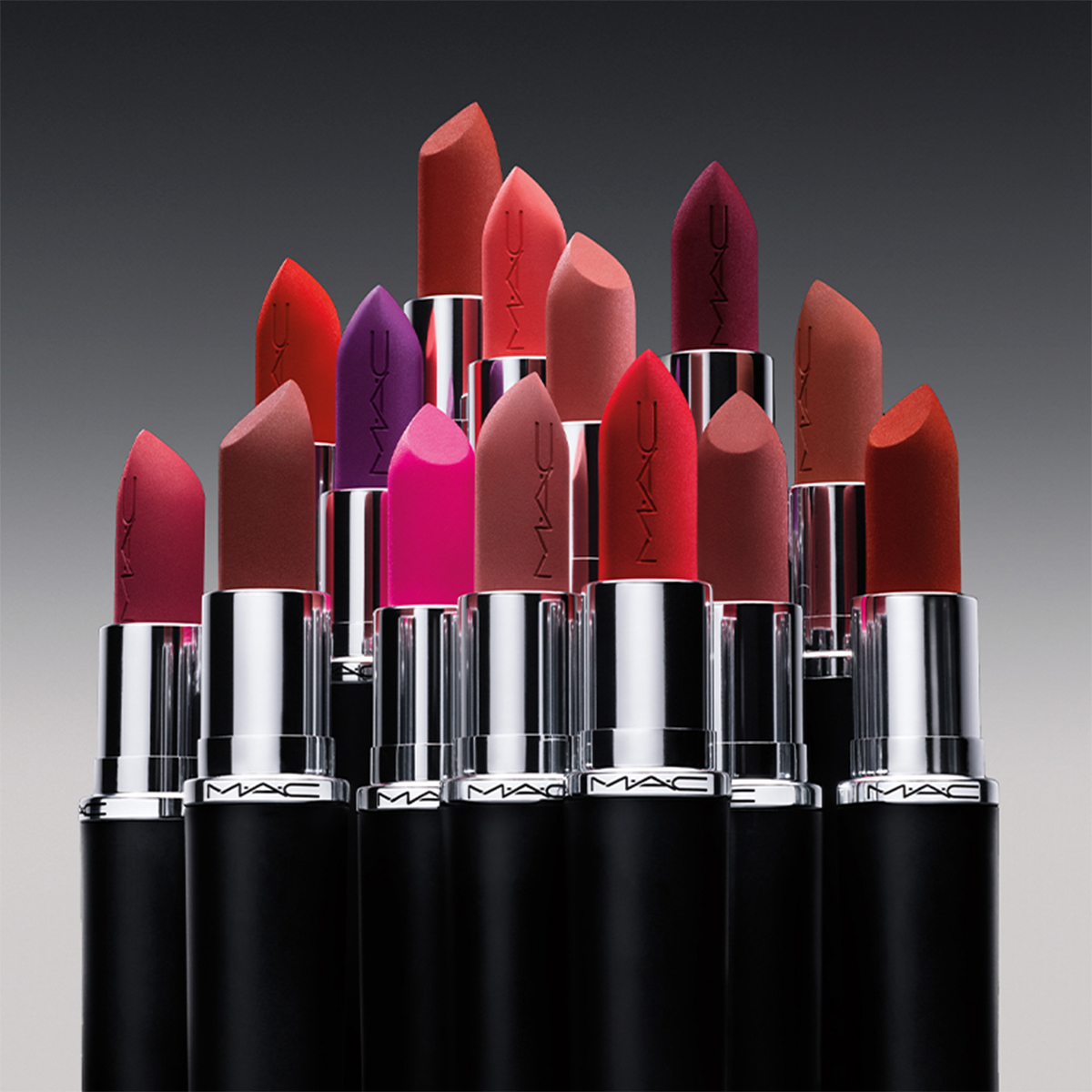 Kahdentoista erivärisen MAC Cosmetics -huulipunan kokoelma on rivissä tummanharmaalla taustalla. Pakkaus on musta, ja siinä on hopeisia yksityiskohtia, ja MAC-logo näkyy selvästi jokaisessa huulipunassa.