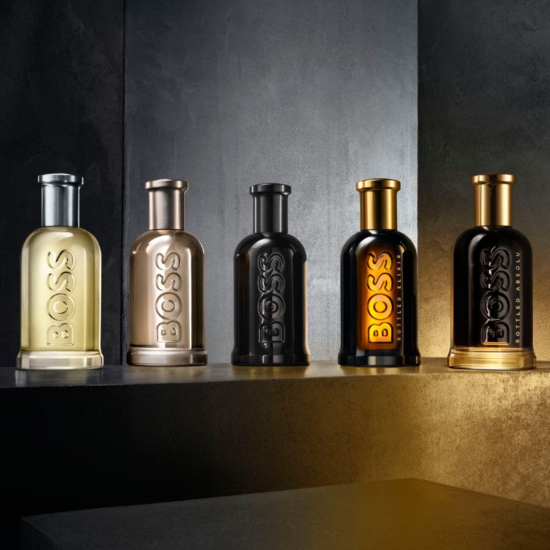 Fem flasker med Hugo Boss parfyme i forskjellige farger og design, plassert på en mørk overflate.