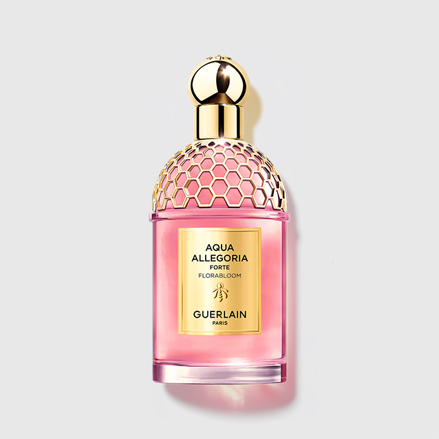 Guerlain Aqua Allegoria Forte Flora Bloom parfym i en rosa flaska med guldfärgad bikakemönstrad kork och etikett. På flaskan står “AQUA ALLEGORIA FORTE FLORA BLOOM GUERLAIN PARIS”.