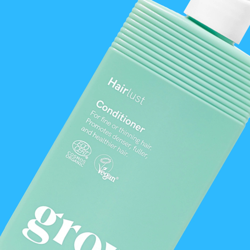 Grön tub med hårvård från Hairlust mot blå bakgrund. På förpackningen syns texterna ”Hairlust”, ”Conditioner”, ”For fine or thinning hair. Promotes denser, fuller and healthier hair.” samt symbolerna ”COSMOS ORGANIC” och ”Vegan”.