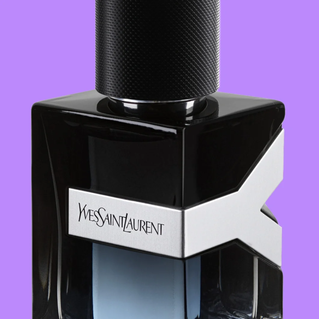 Närbild av Yves Saint Laurent-parfym i en svart glasflaska med silverfärgad YSL-detalj och texten ”Yves Saint Laurent”, mot lila bakgrund.