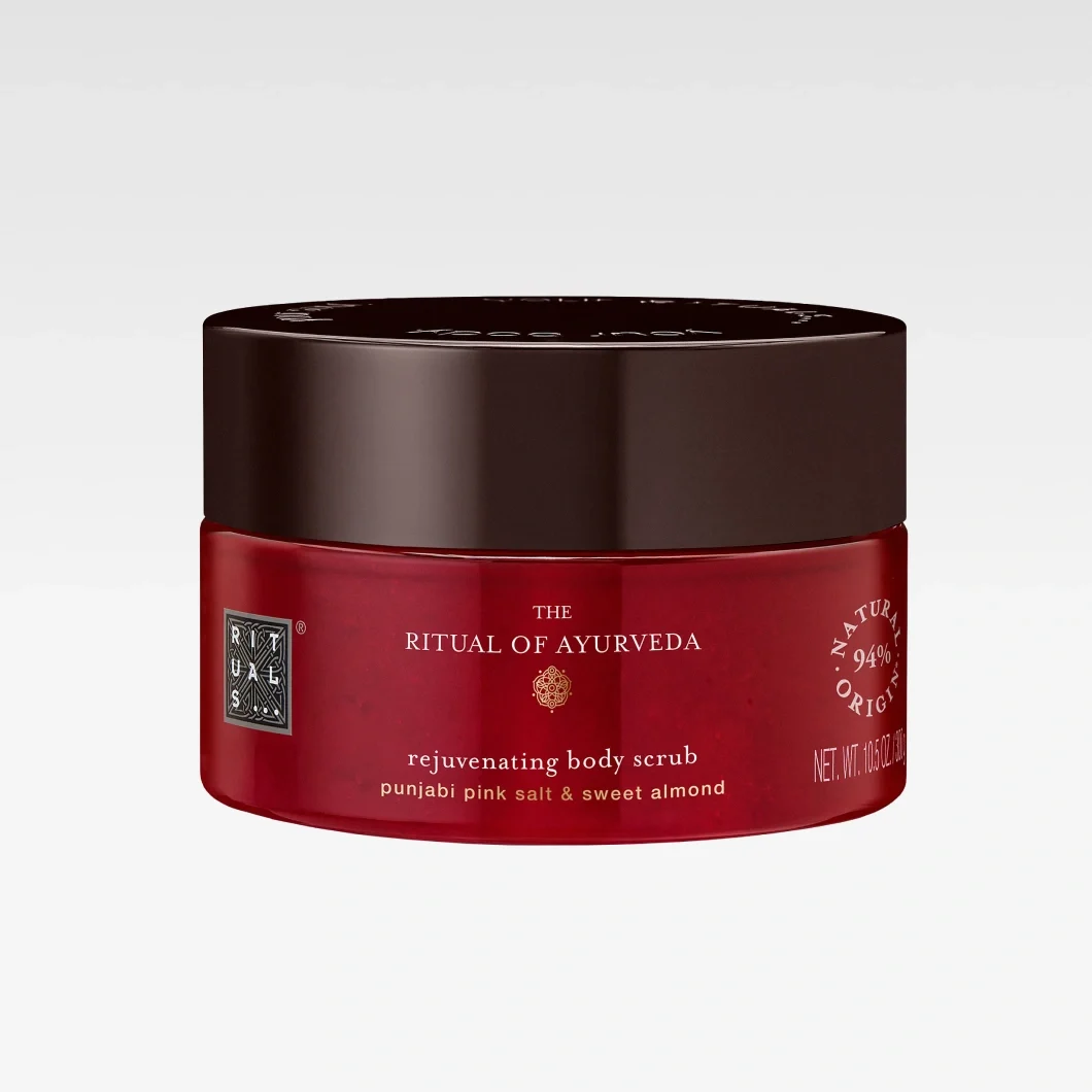 Röd burk från Rituals The Ritual of Ayurveda rejuvenating body scrub med mörkbrunt lock. Texten “punjabi pink salt & sweet almond” och “94% natural origin” syns på kroppsskrubben.