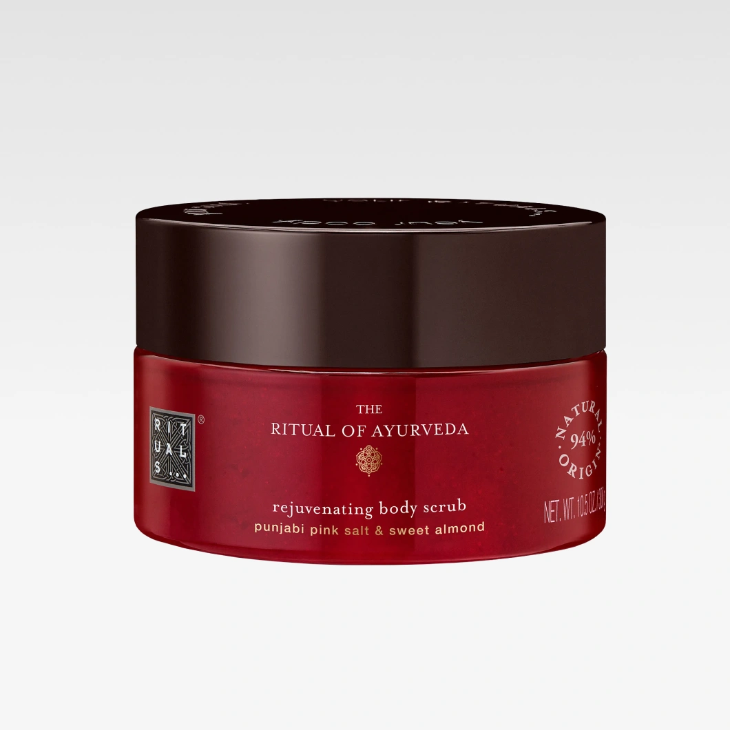 Punainen Rituals The Ritual of Ayurveda rejuvenating body scrub -vartalokuorinta tummanruskealla kannella. Pakkauksessa näkyvät tekstit “punjabi pink salt & sweet almond” ja “94% natural origin”.