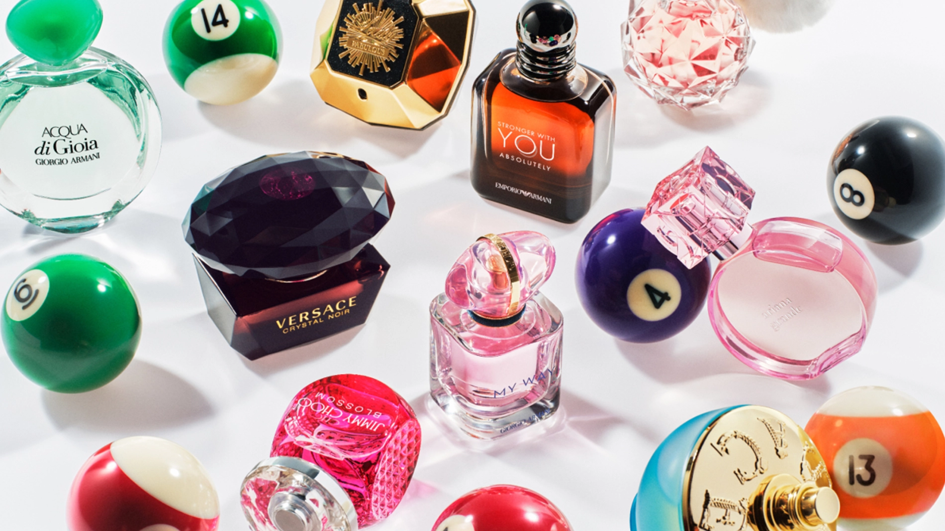 Bilde som viser flere parfymeflasker arrangert blant biljardkuler. Parfymene inkluderer Acqua di Gioia fra Giorgio Armani, Versace Crystal Noir, Stronger With You Intensely fra Emporio Armani, My Way fra Giorgio Armani, og andre. Bakgrunnen er hvit.