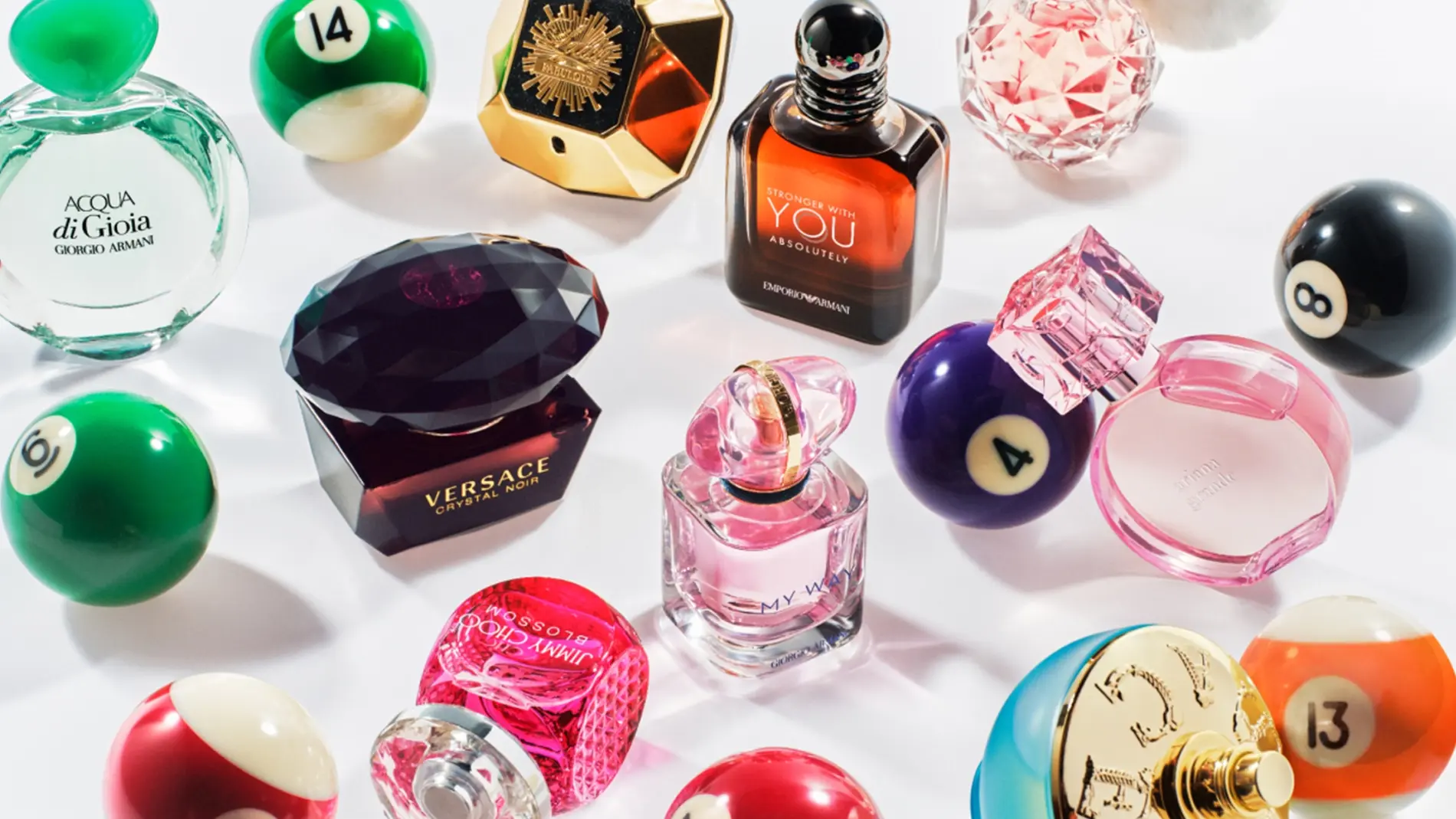 Kuva, joka näyttää useita hajuvesipulloja järjestettynä biljardipallojen joukkoon. Hajusteet sisältävät Acqua di Gioia Giorgio Armanilta, Versace Crystal Noir, Stronger With You Intensely Emporio Armanilta, My Way Giorgio Armanilta, ja muita. Tausta on valkoinen.