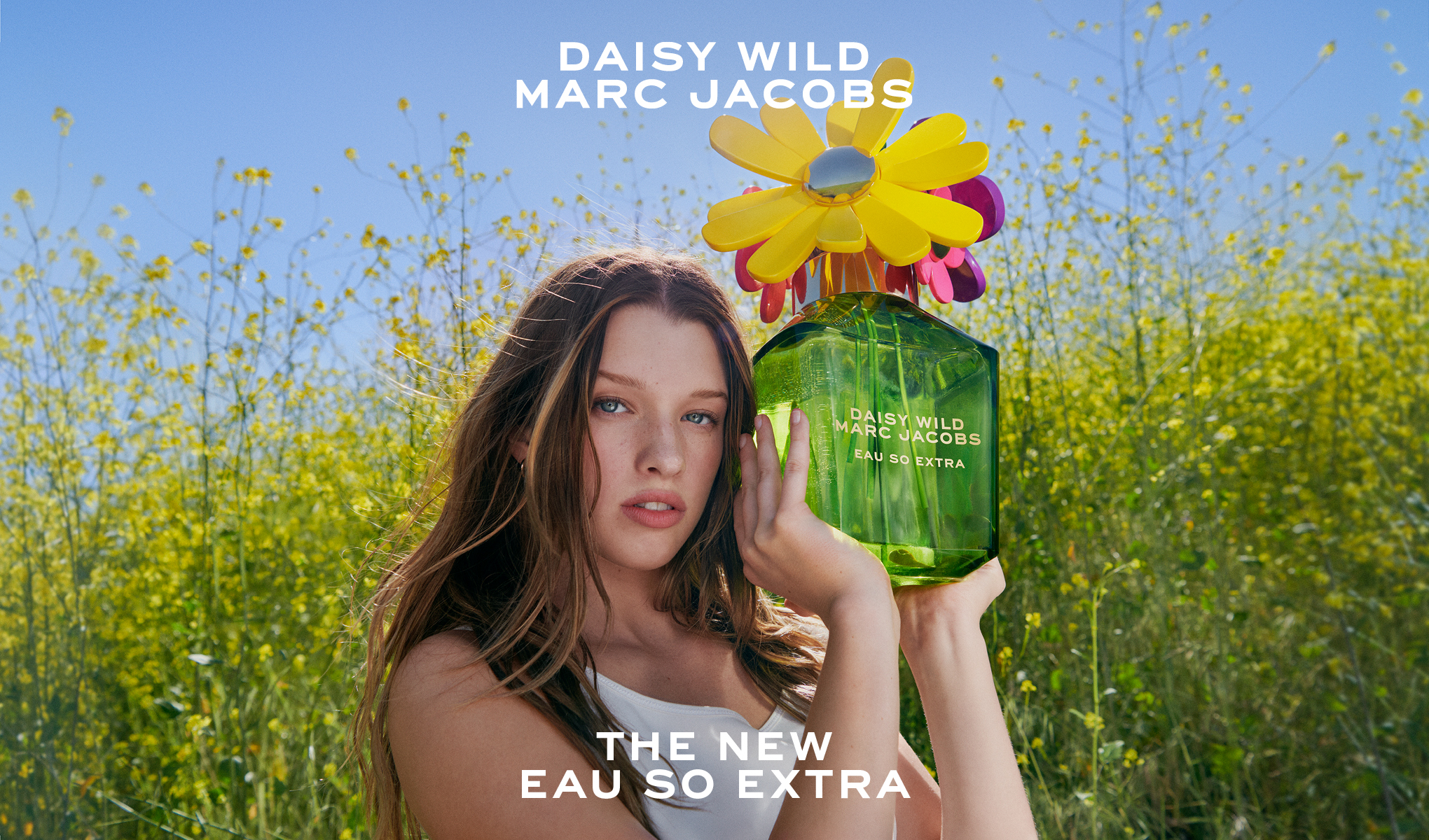 Nainen pitelee Daisy Wild Marc Jacobs -hajuvesipulloa kukkivassa maisemassa.