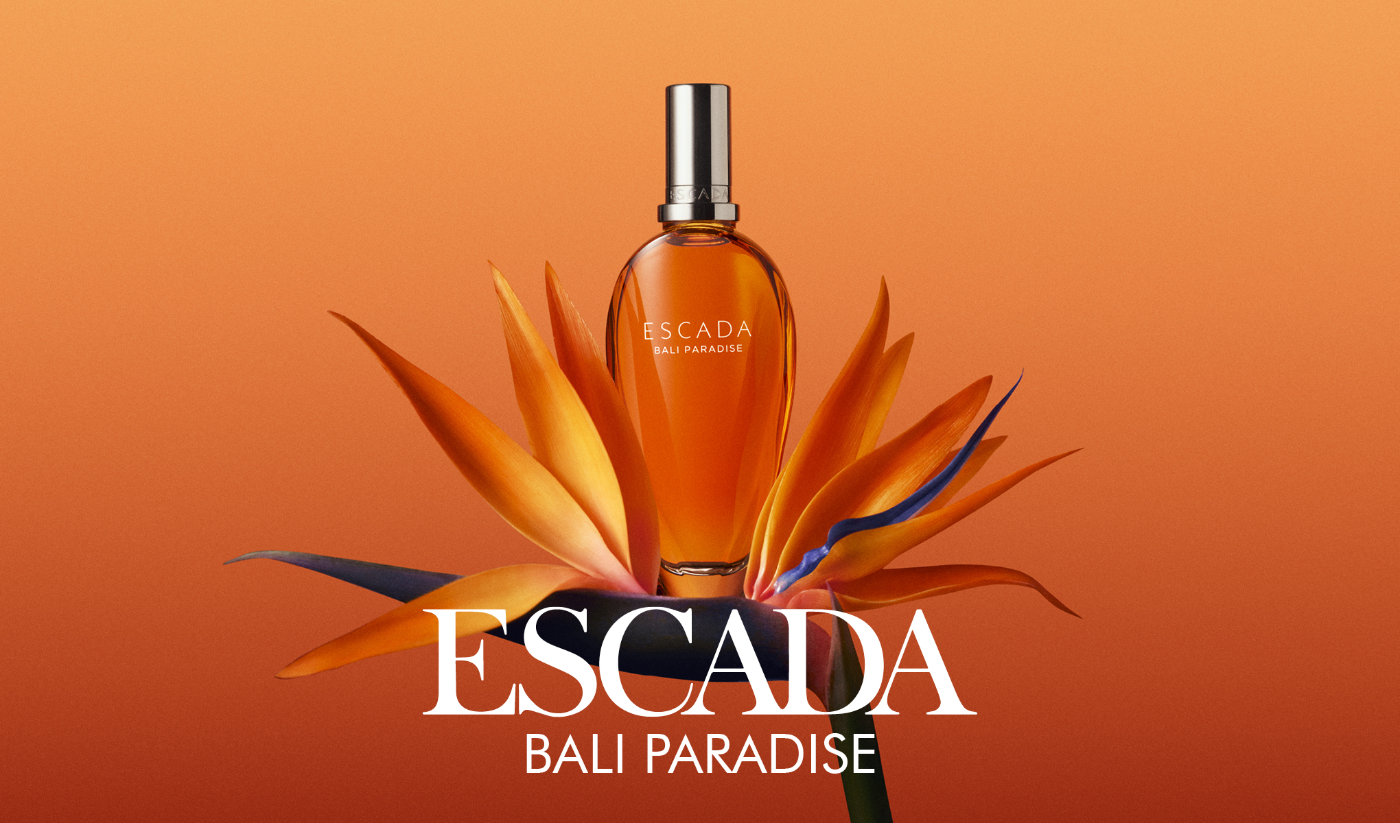 Hajuvesipullo ”Escada Bali Paradise” on sijoitettu oranssiin kukkaan oranssia taustaa vasten. Pullon alapuolella näkyy teksti ”Escada Bali Paradise”.