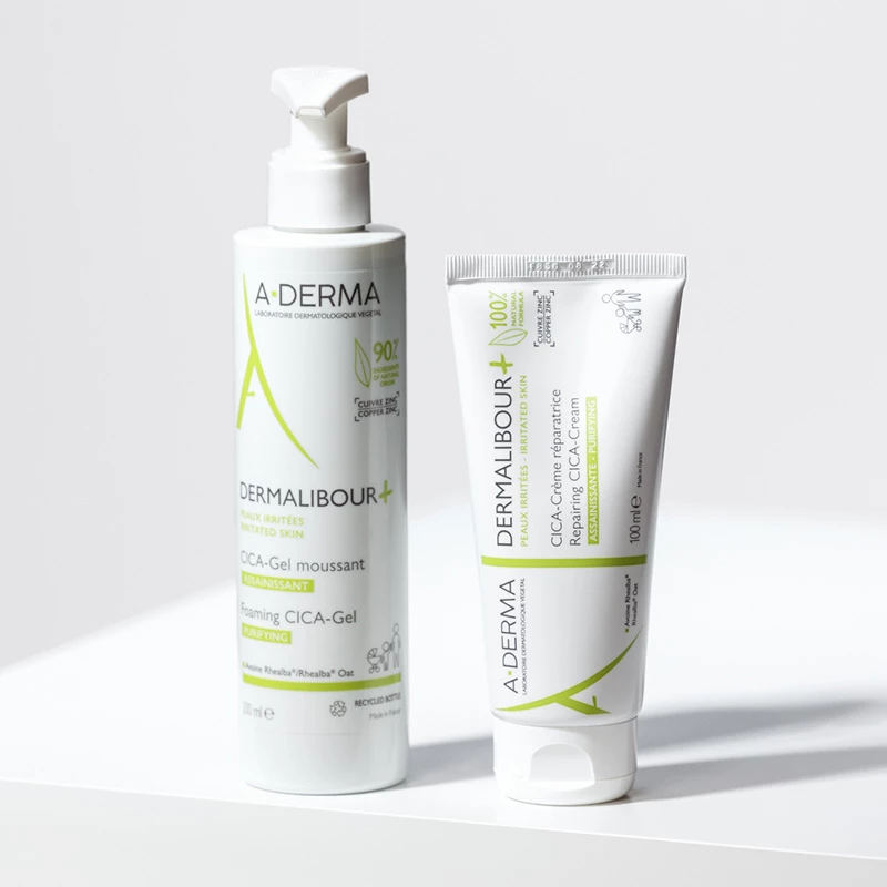 Bilden visar två hudvårdsprodukter från märket A-Derma. Båda produkterna har gröna detaljer och är designade för irriterad hud. Bakgrunden är ljus och enkel, vilket framhäver produkterna.