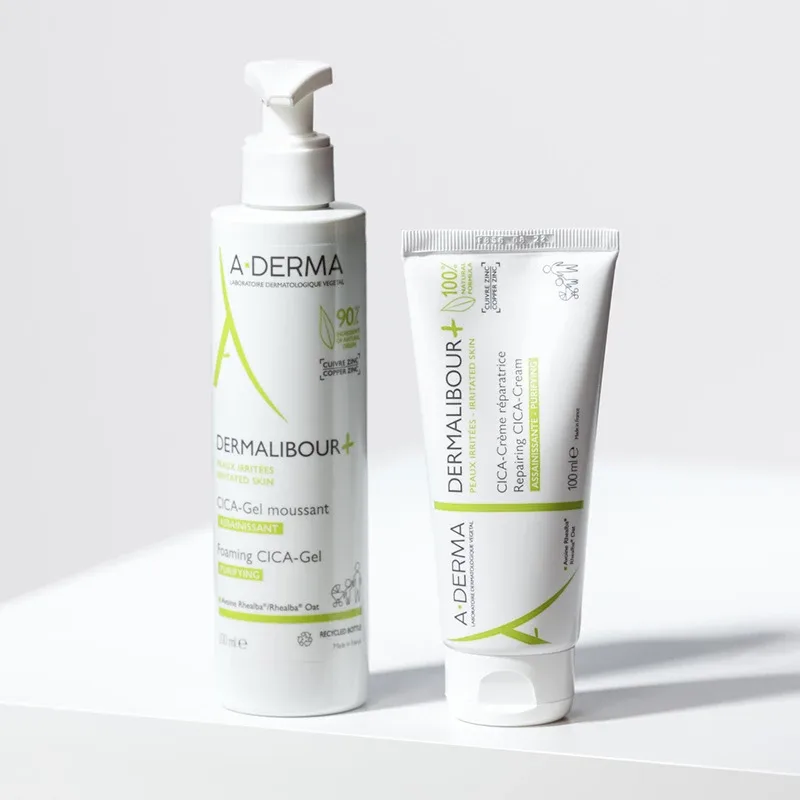 Bilden visar två hudvårdsprodukter från märket A-Derma. Båda produkterna har gröna detaljer och är designade för irriterad hud. Bakgrunden är ljus och enkel, vilket framhäver produkterna.