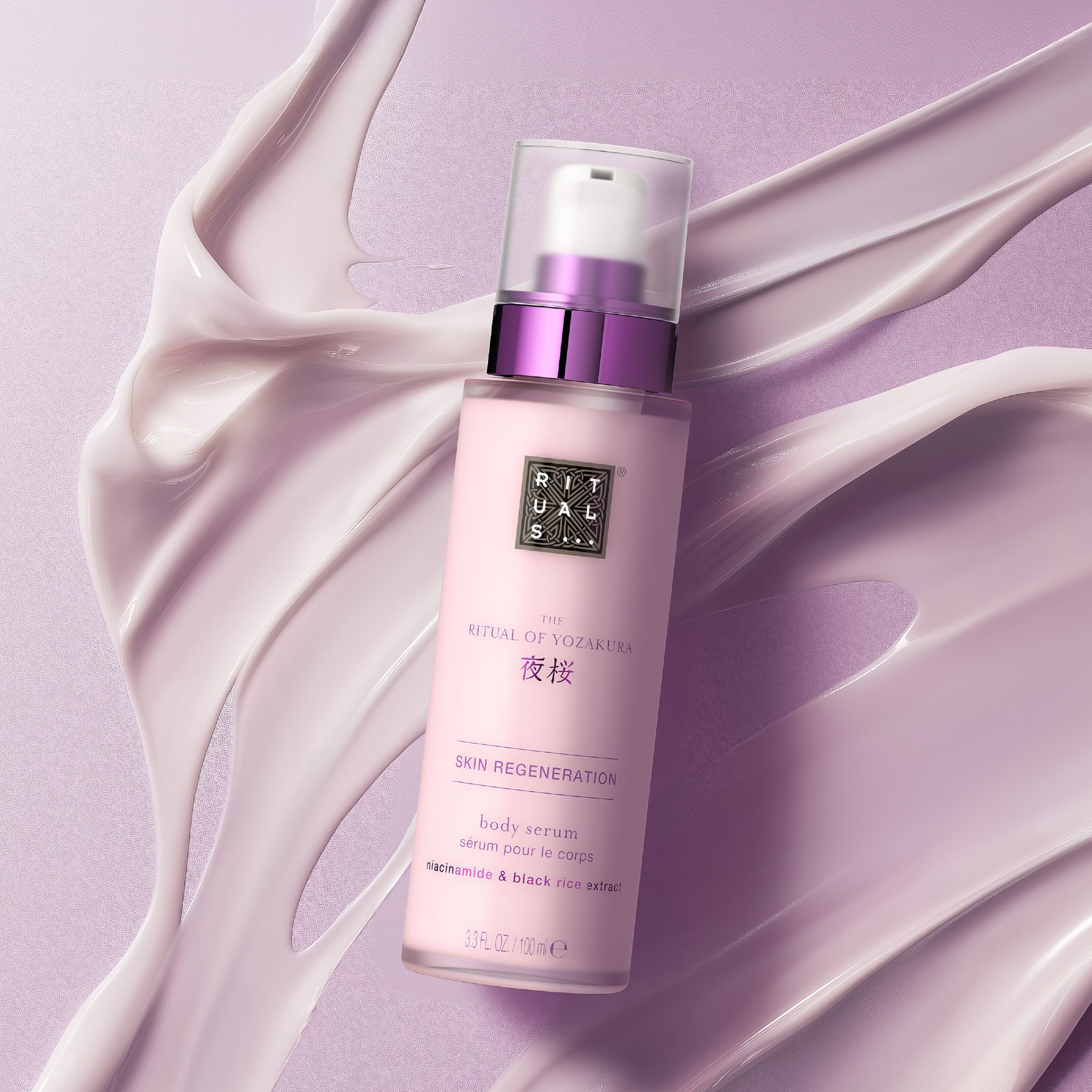 Rituals The Ritual of Yozakura Skin Regeneration body serum ligger mot svepande krämtextur i ljuslila toner. På flaskan syns Rituals-logotypen samt texten “THE RITUAL OF YOZAKURA”, “SKIN REGENERATION”, “body serum” och “niacinamide & black rice extract”.