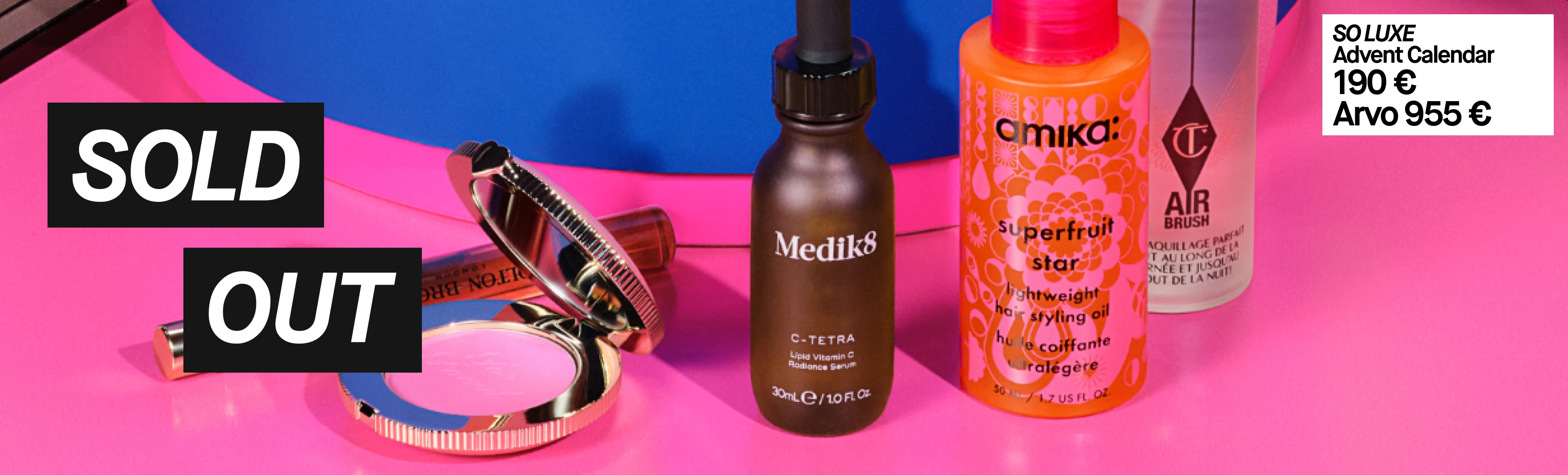 Kauneustuotteita pinkillä ja sinisellä taustalla. Pinkki puuterirasia ja huulipuna on merkitty 'SOLD OUT' (loppuunmyyty). Muita tuotteita ovat: Medik8 C-Tetra Lipid Vitamin C Radiance Serum, Amika Superfruit Star Lightweight Hair Styling Oil ja Charlotte Tilbury Airbrush -suihke. Valkoisessa tarrassa lukee: 'SO LUXE Advent Calendar 190 € Arvo 955 €'.