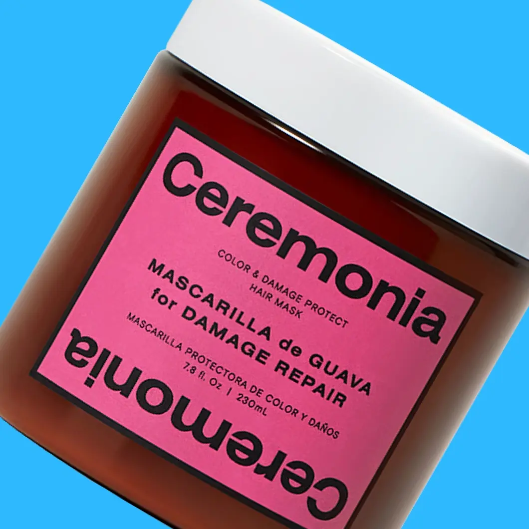 Ceremonia Color & Damage Protect Hair Mask i brun krukke med rosa etikett mot blå bakgrunn. På emballasjen vises tekstene «Ceremonia», «COLOR & DAMAGE PROTECT HAIR MASK», «MASCARILLA de GUAVA for DAMAGE REPAIR», «MASCARILLA PROTECTORA DE COLOR Y DAÑOS» og «230 mL».
