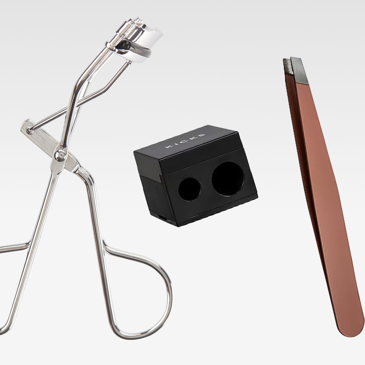 Sminkverktyg mot vit bakgrund: metallisk ögonfransböjare, svart dubbel pennvässare och sned pincett.